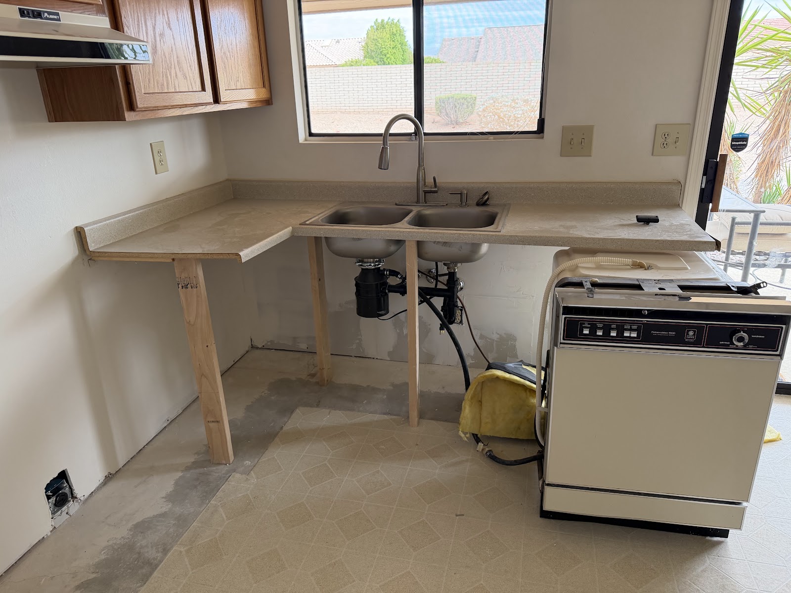 Sink wall of a 1980s kitchen with the old oak cabinets removed and the counter propped, before new cabinets are set