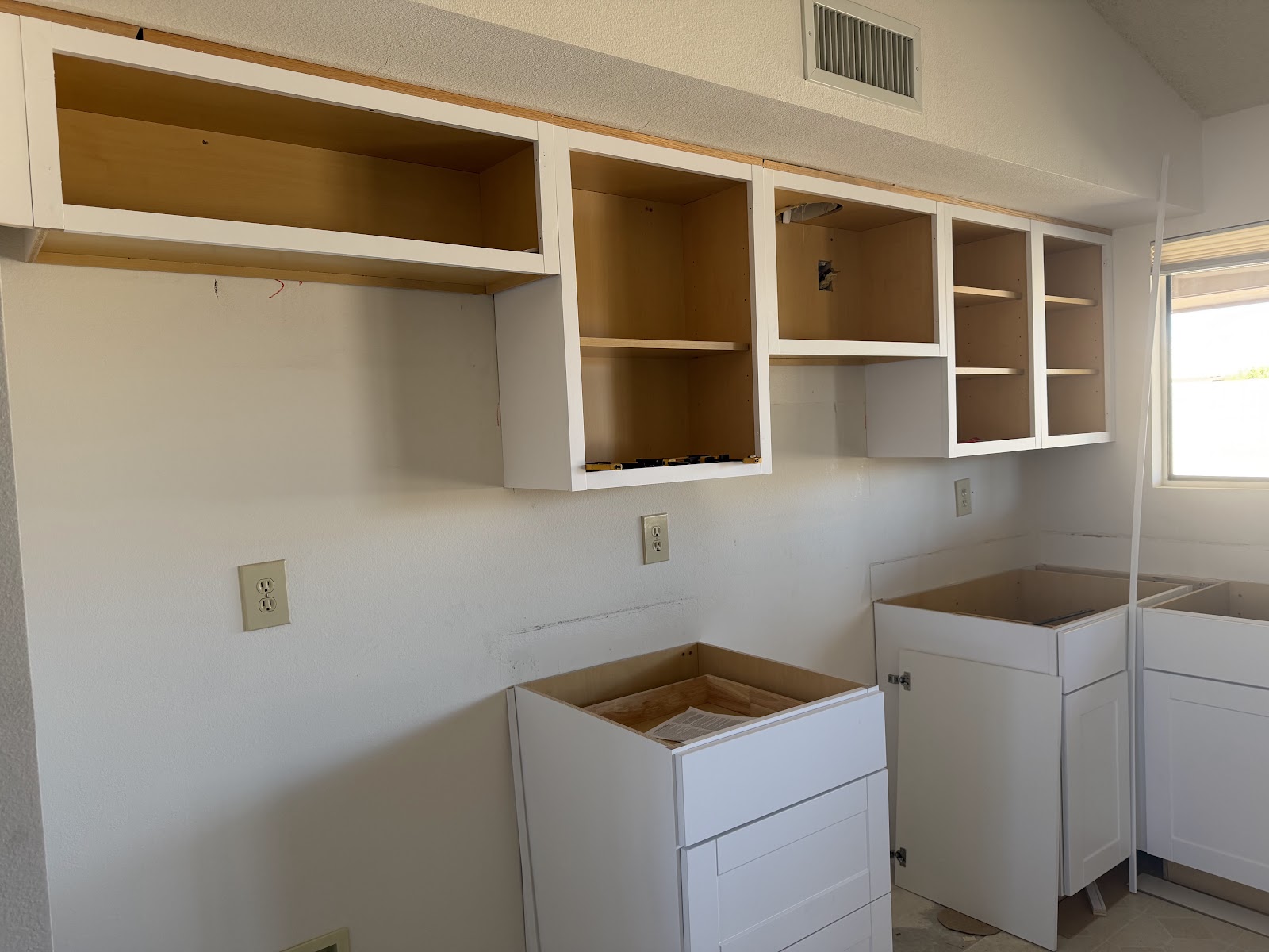 New white Shaker upper cabinets hung under a kitchen soffit with the doors off during installation