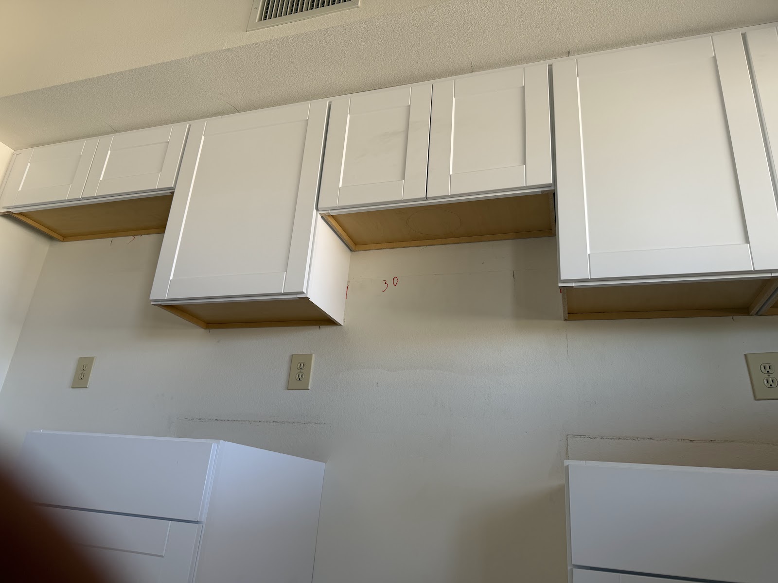 Close view of satin white Shaker uppers set tight under a soffit with a 30 inch range hood opening