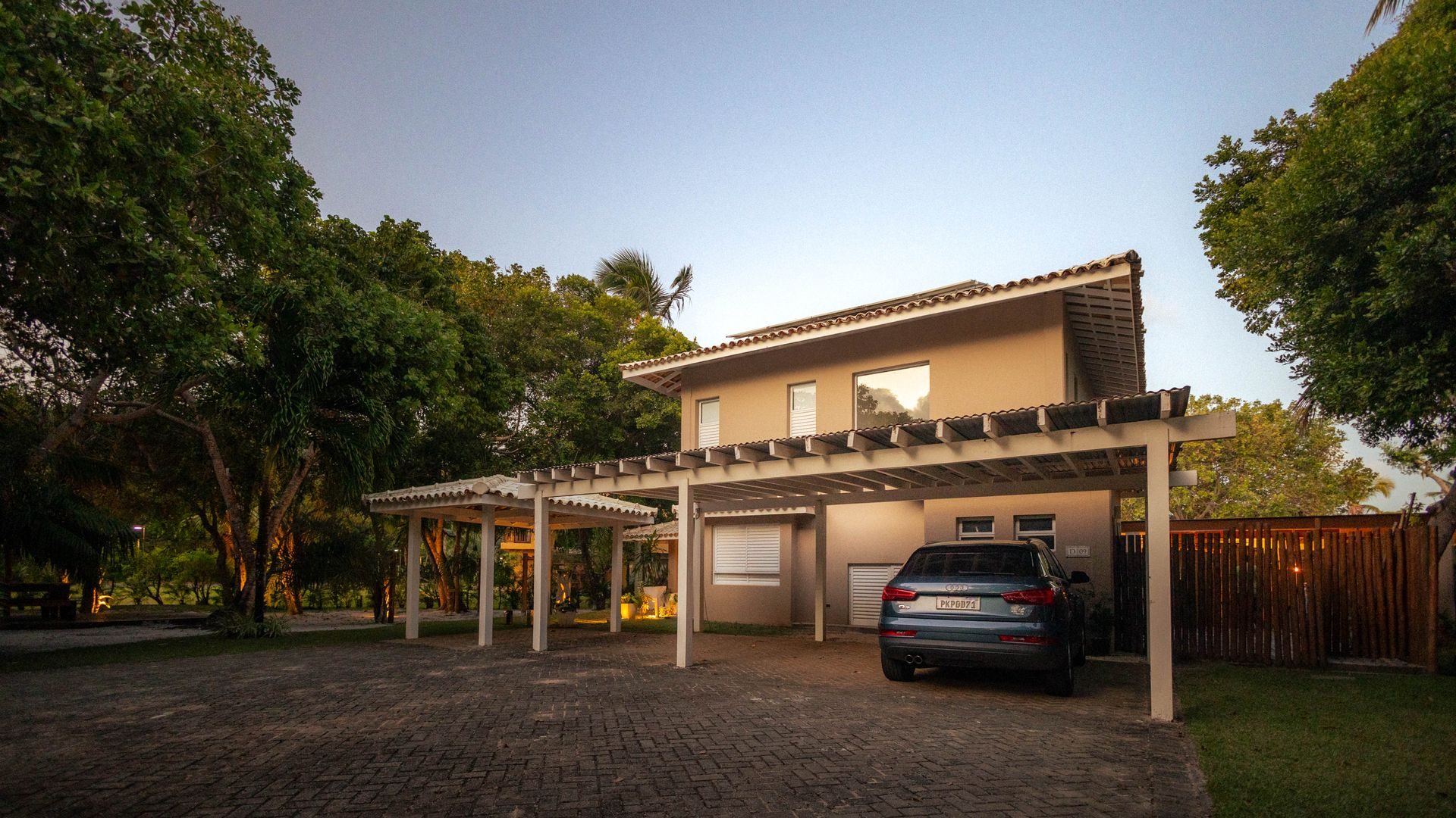 A clean attached carport on a stucco home with a tile roof and a car parked underneath