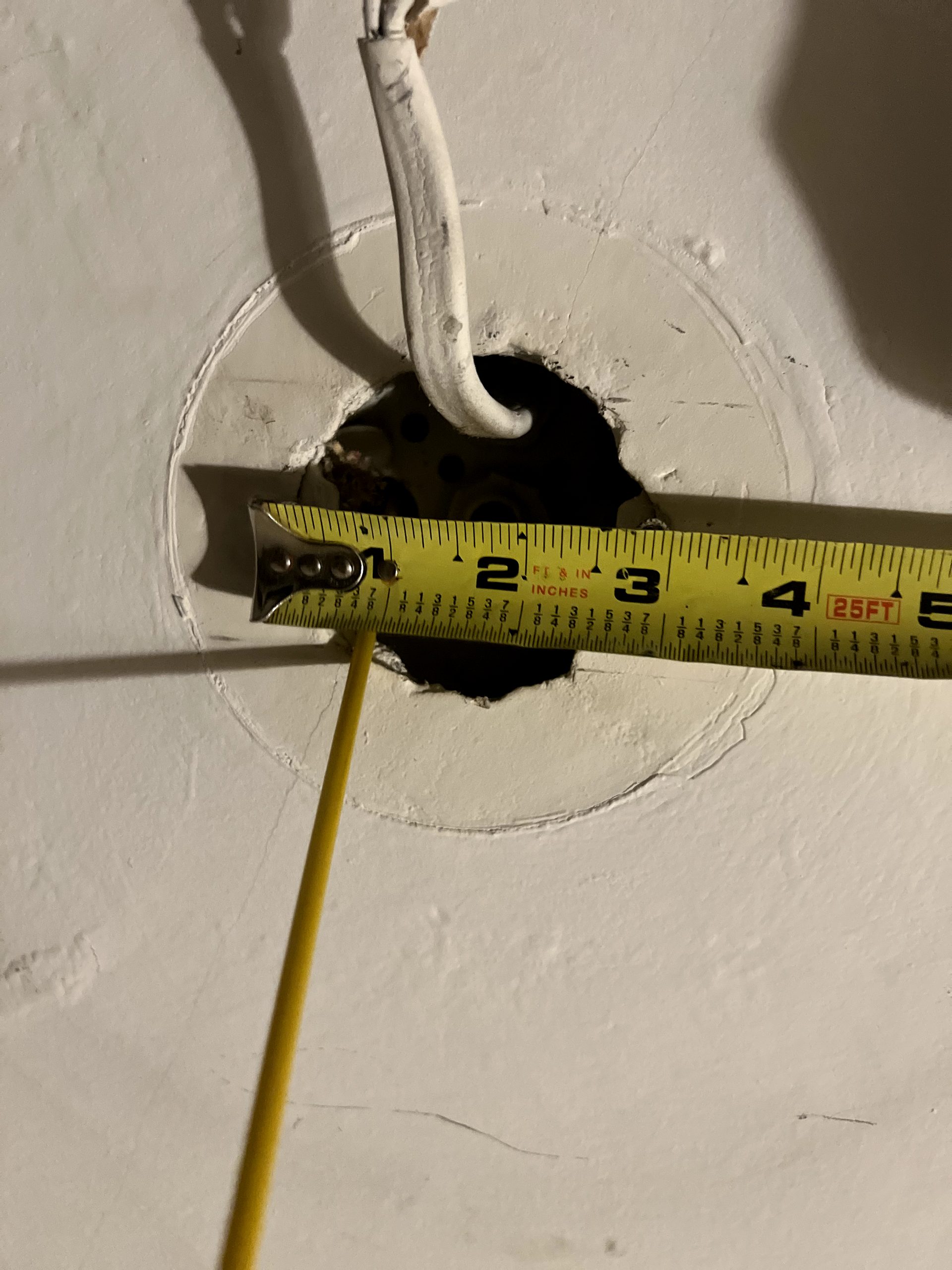 Measuring the ceiling opening to verify the electrical box before hanging a ceiling fan