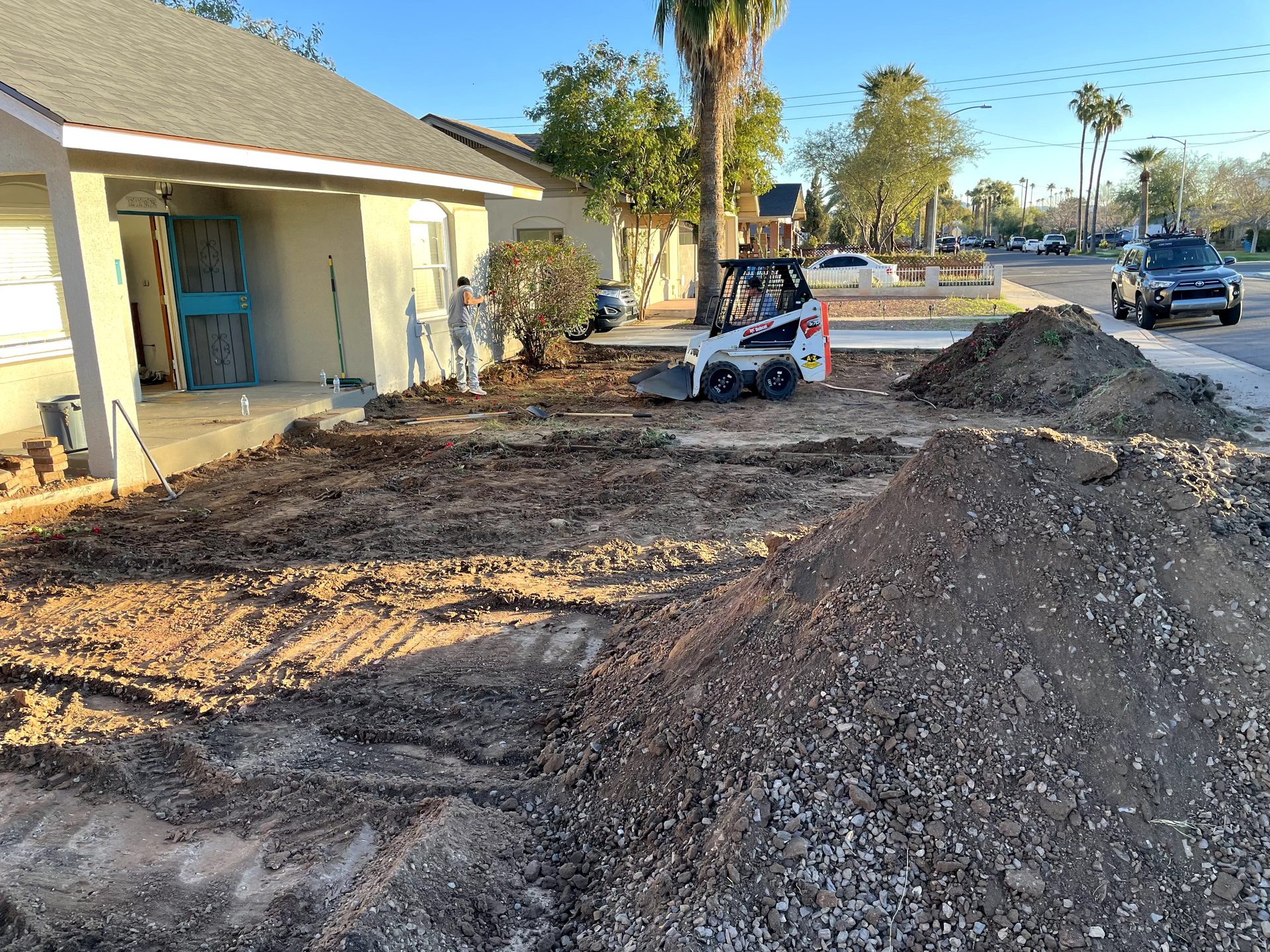Compact skid steer grading the front yard during a desert landscaping conversion in Phoenix