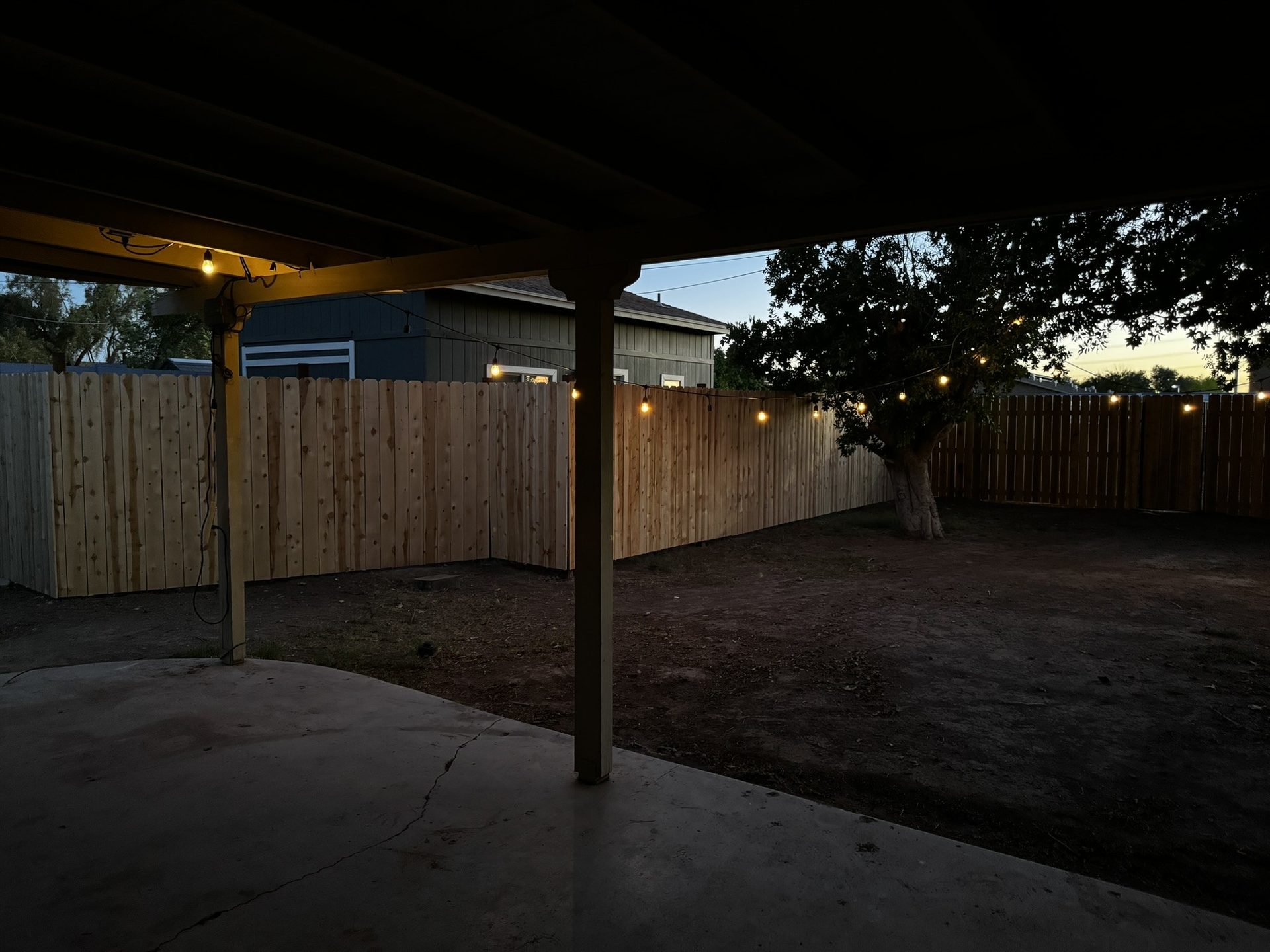Wood dividing fence in a Tempe backyard lit by string lights after dark