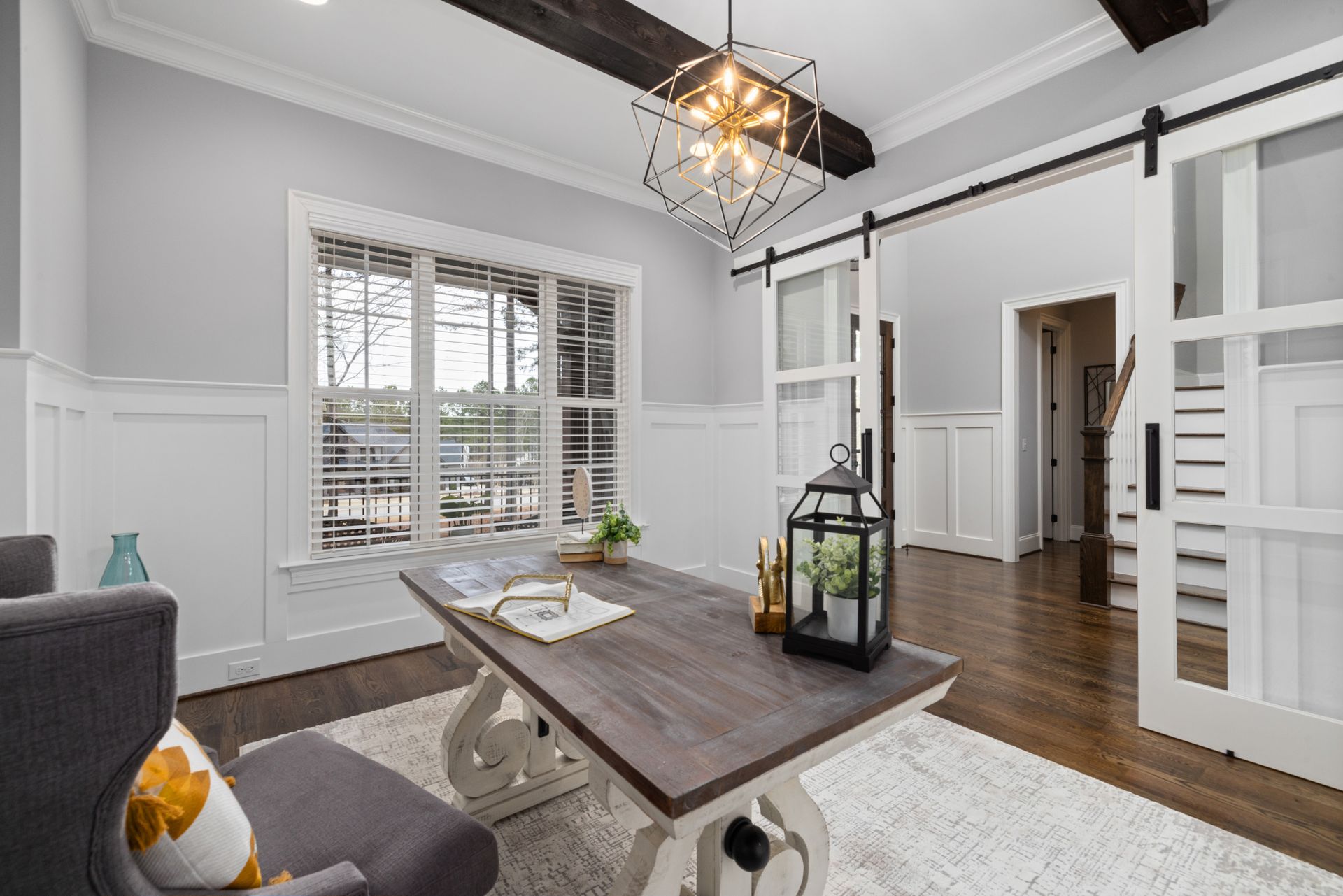 Pair of white sliding barn doors with glass panels on one long black flat-track rail across a wide opening from a home office to the front hall
