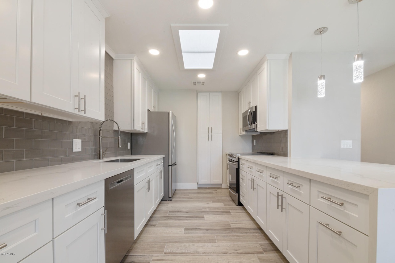 Flower Main House kitchen remodel in Phoenix: white shaker cabinets, quartz countertops, grey glass subway tile backsplash and a skylight over the galley run