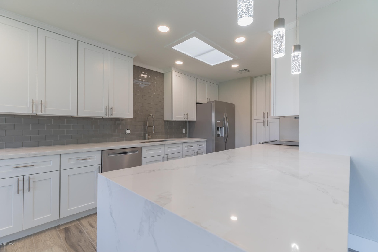 Flower Main House kitchen remodel in Phoenix: waterfall quartz island with a marble-look vein, seeded-glass pendant lights and stainless appliances