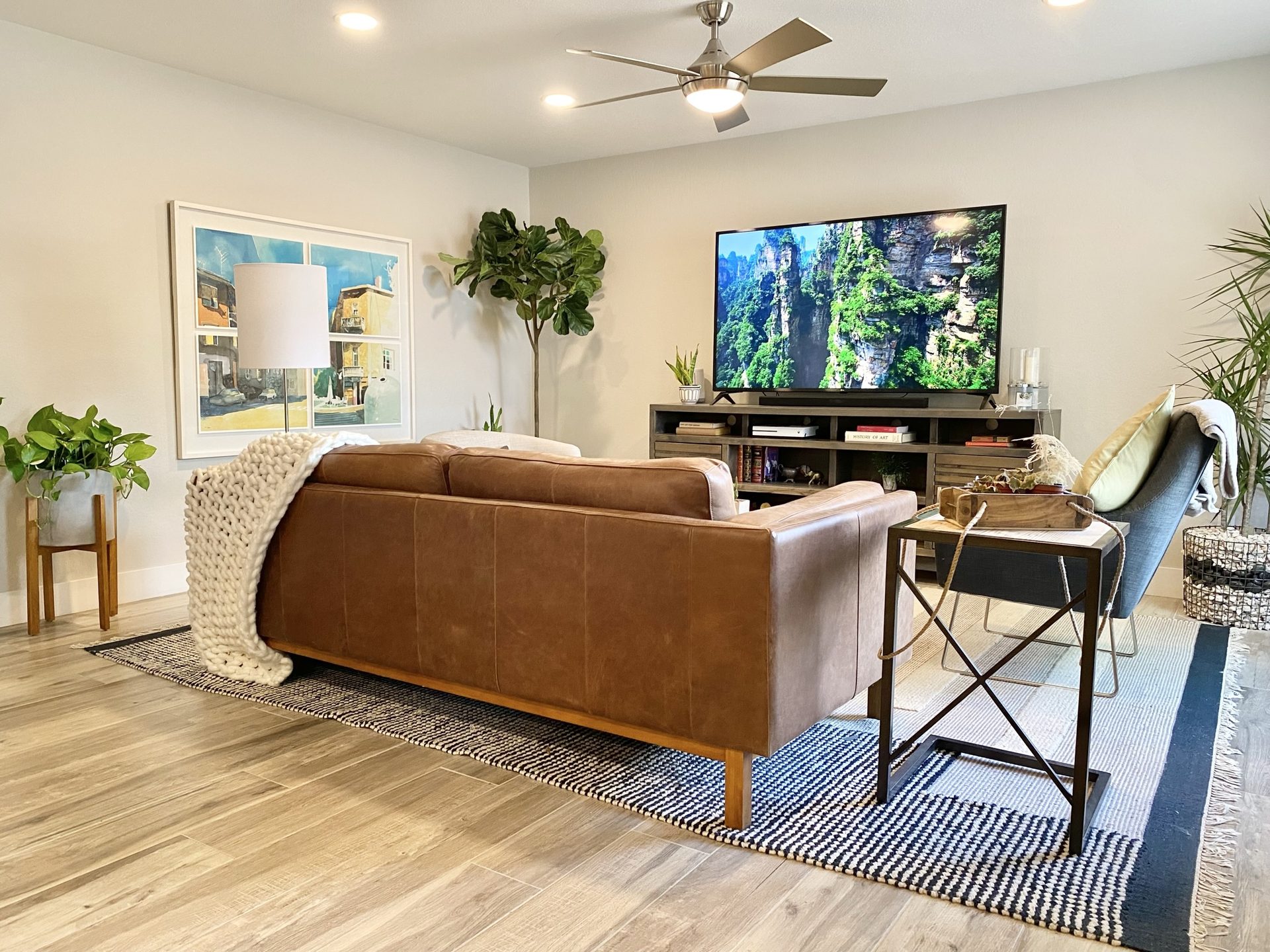 Flower Main House short-term rental in Phoenix: staged living room with a leather sofa, wall-mounted television on a media console, wood-look plank flooring and a ceiling fan