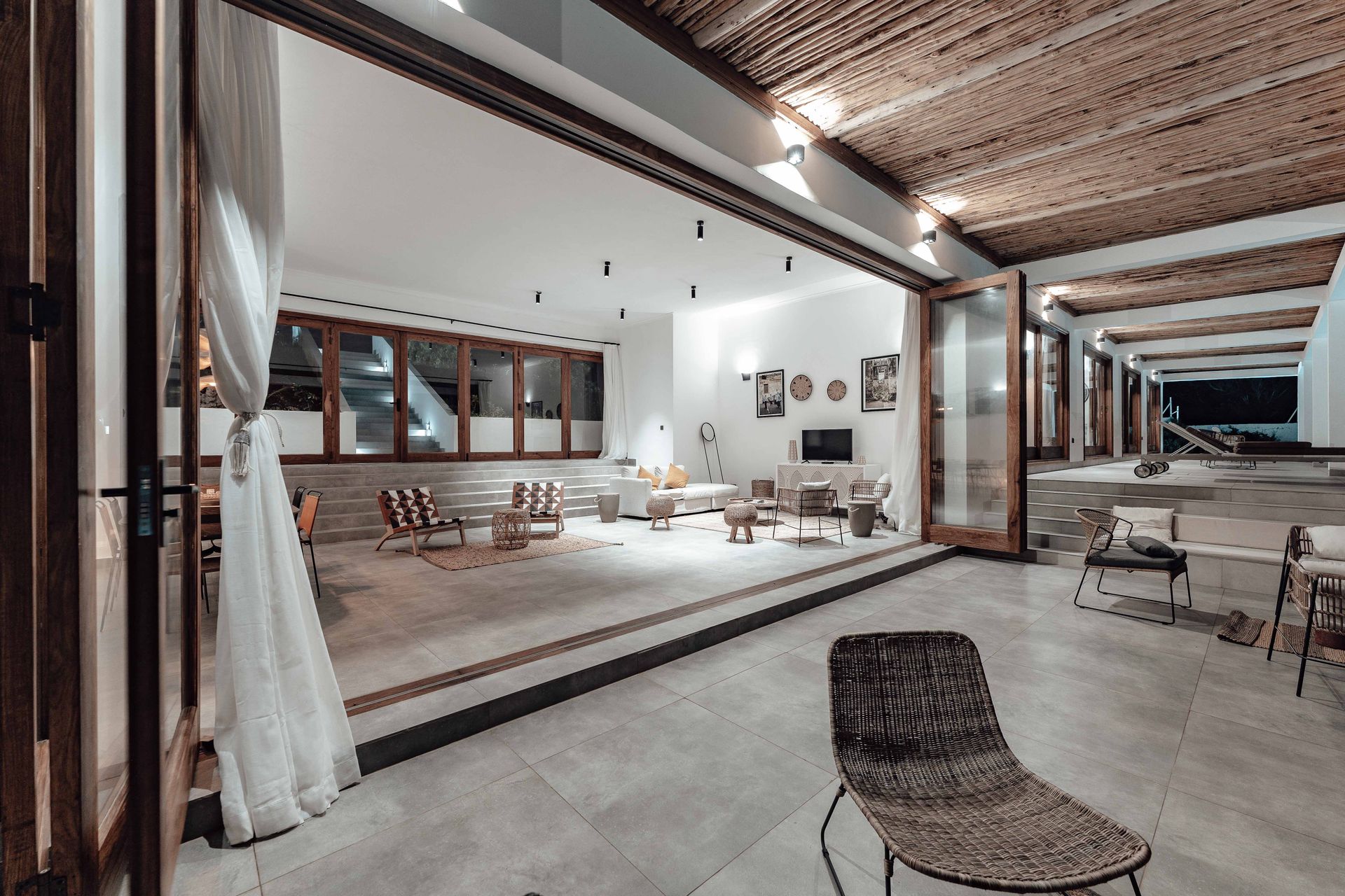 Wood-framed glass folding doors folded back and stacked at one side of a wide opening between a covered patio and a great room