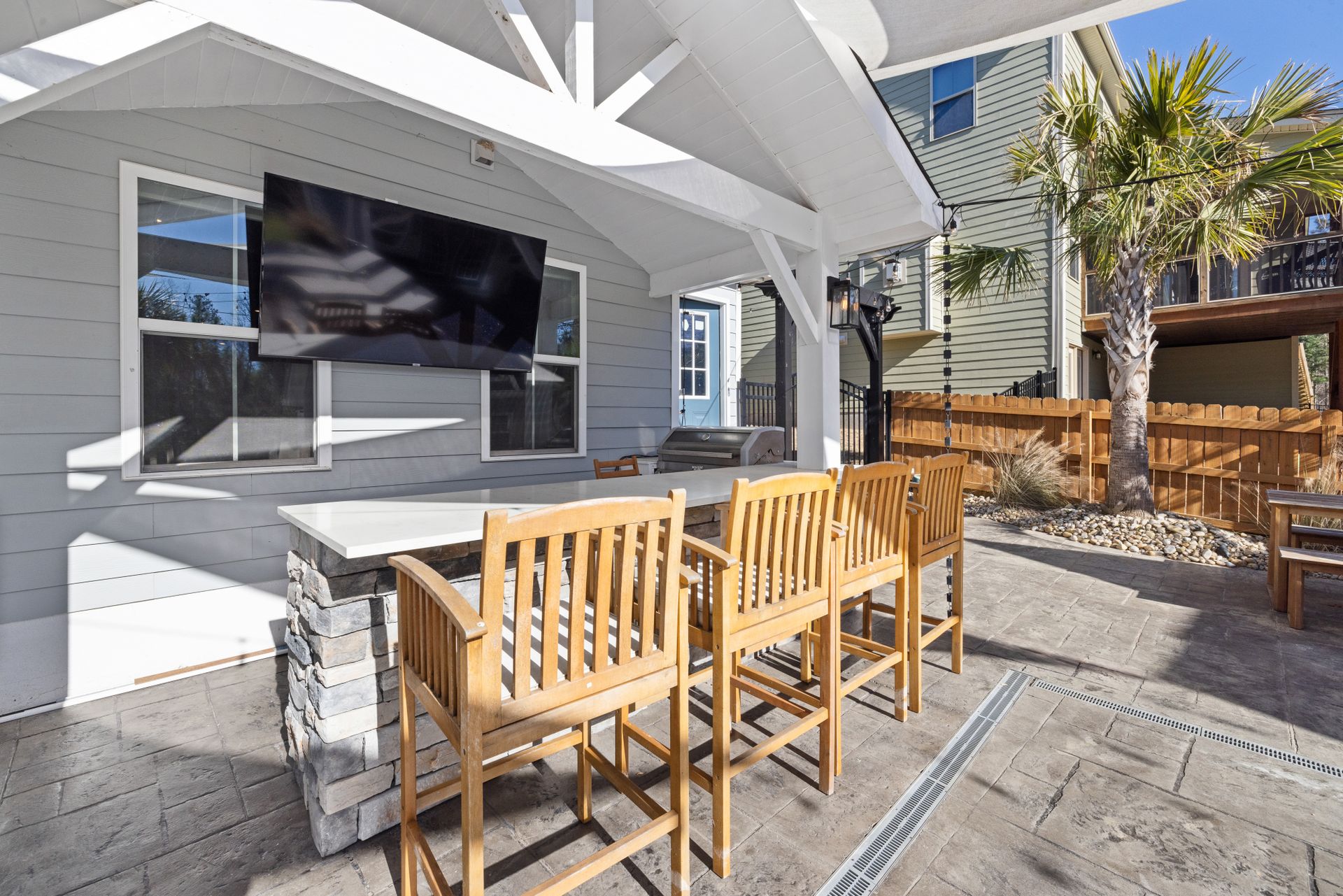 A white-painted gabled wood patio cover on square timber posts with angled knee braces and exposed rafters over an outdoor bar