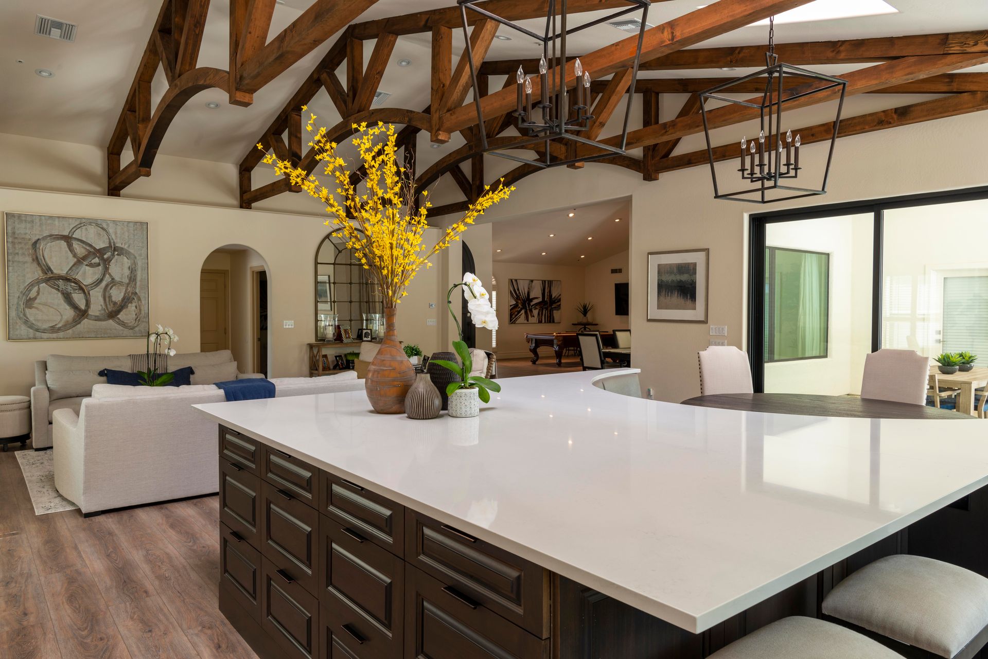 Two black iron lantern chandeliers hanging over a kitchen island in a great room with a vaulted ceiling and dark timber trusses