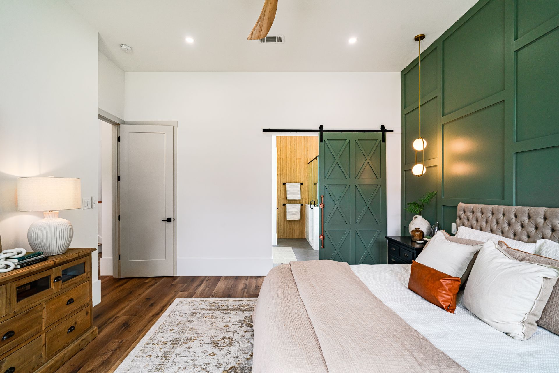 Forest-green sliding barn door with X-pattern panels on a black flat-track rail over a bedroom's bathroom doorway