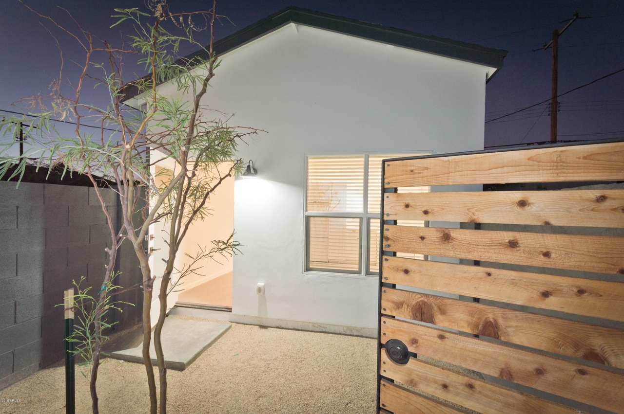 Guest house entry at dusk in Phoenix with a wood slat privacy gate and lit window