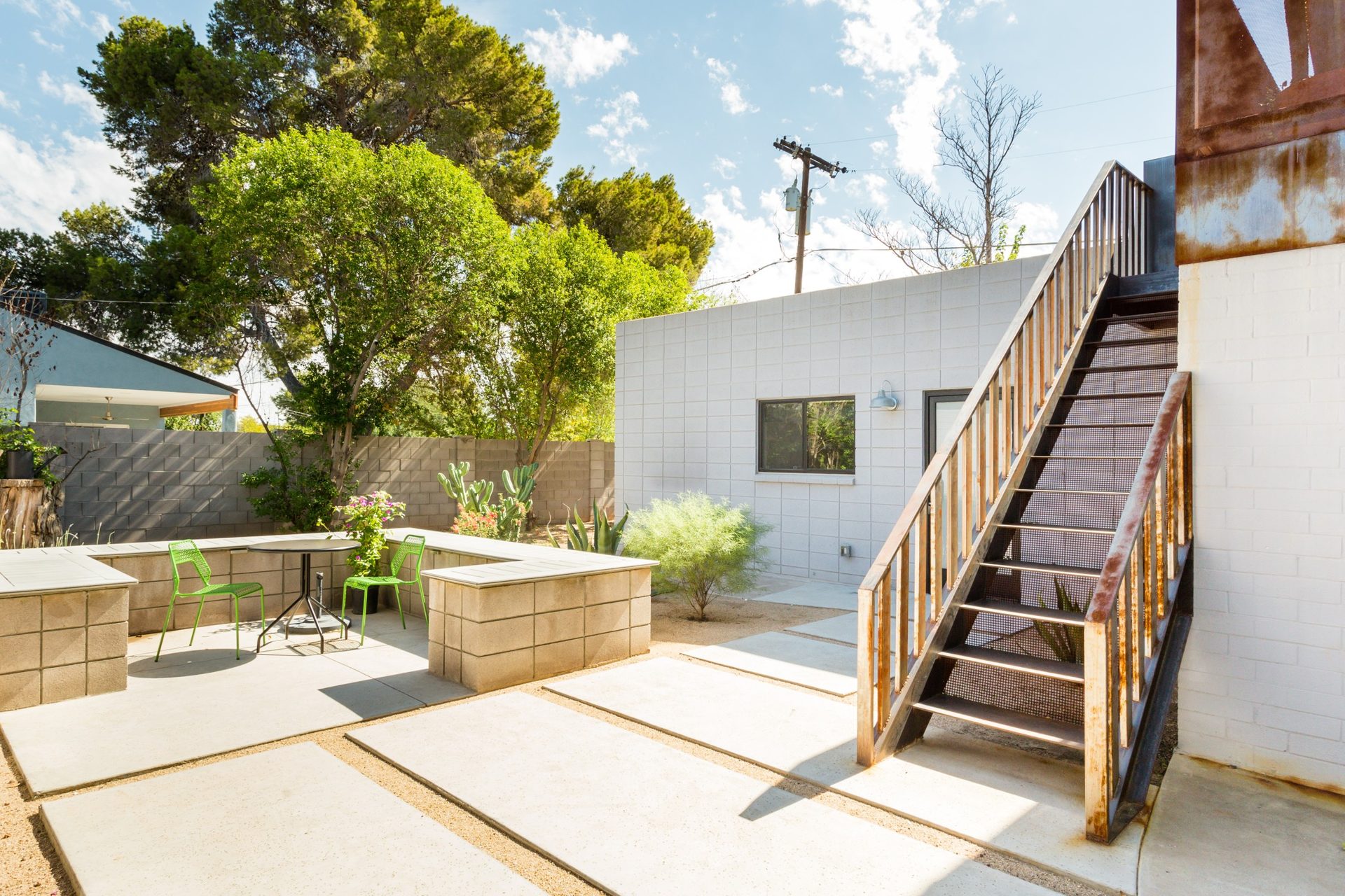 Guest house patio in Phoenix with poured concrete pads, block bench seating and a steel stair to a roof deck