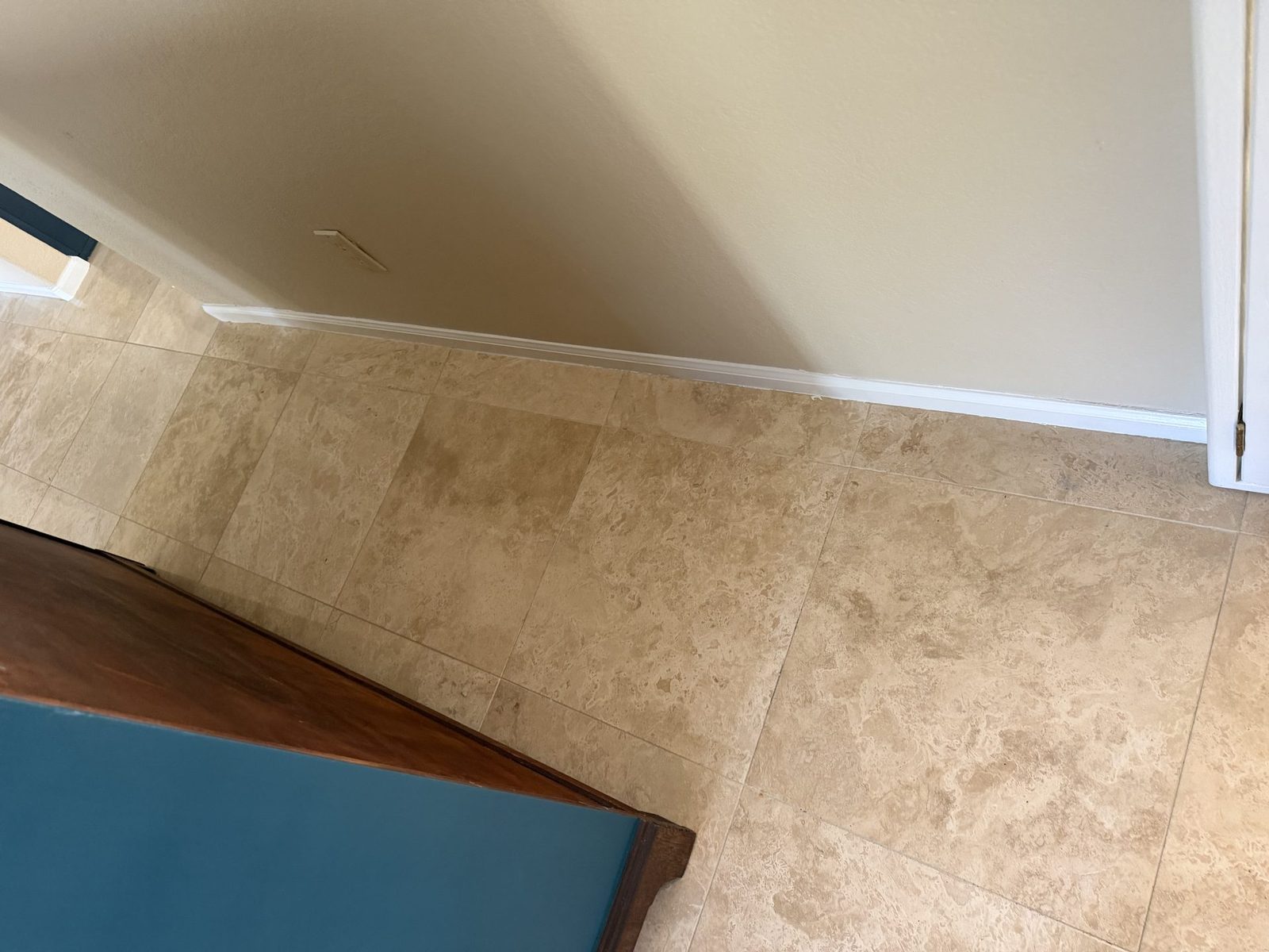 Freshly repainted white baseboard meeting travertine tile, with afternoon light raking across the textured wall above it