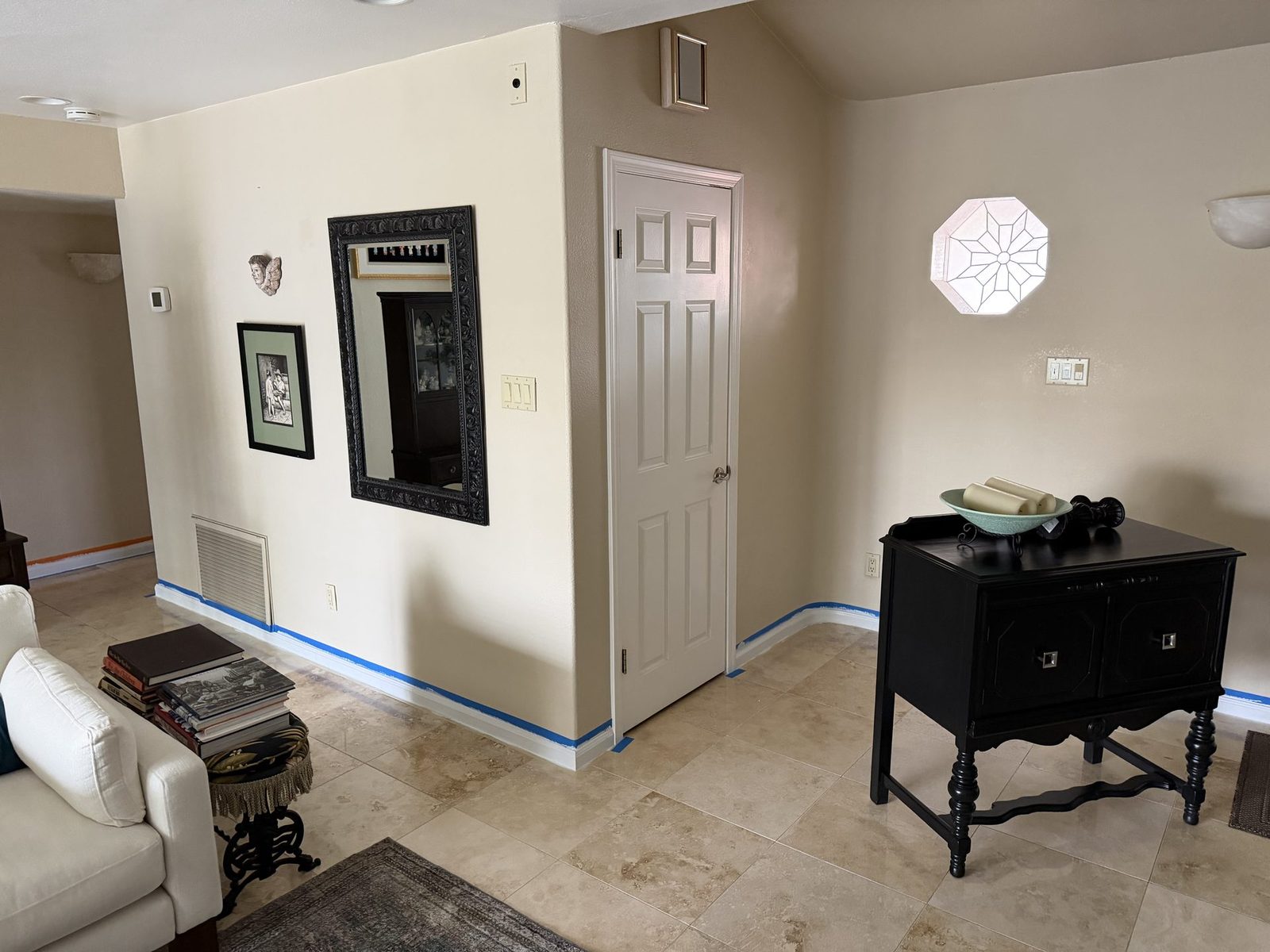 Furnished Phoenix living room with blue painter's tape masking the baseboards along a travertine floor before interior painting