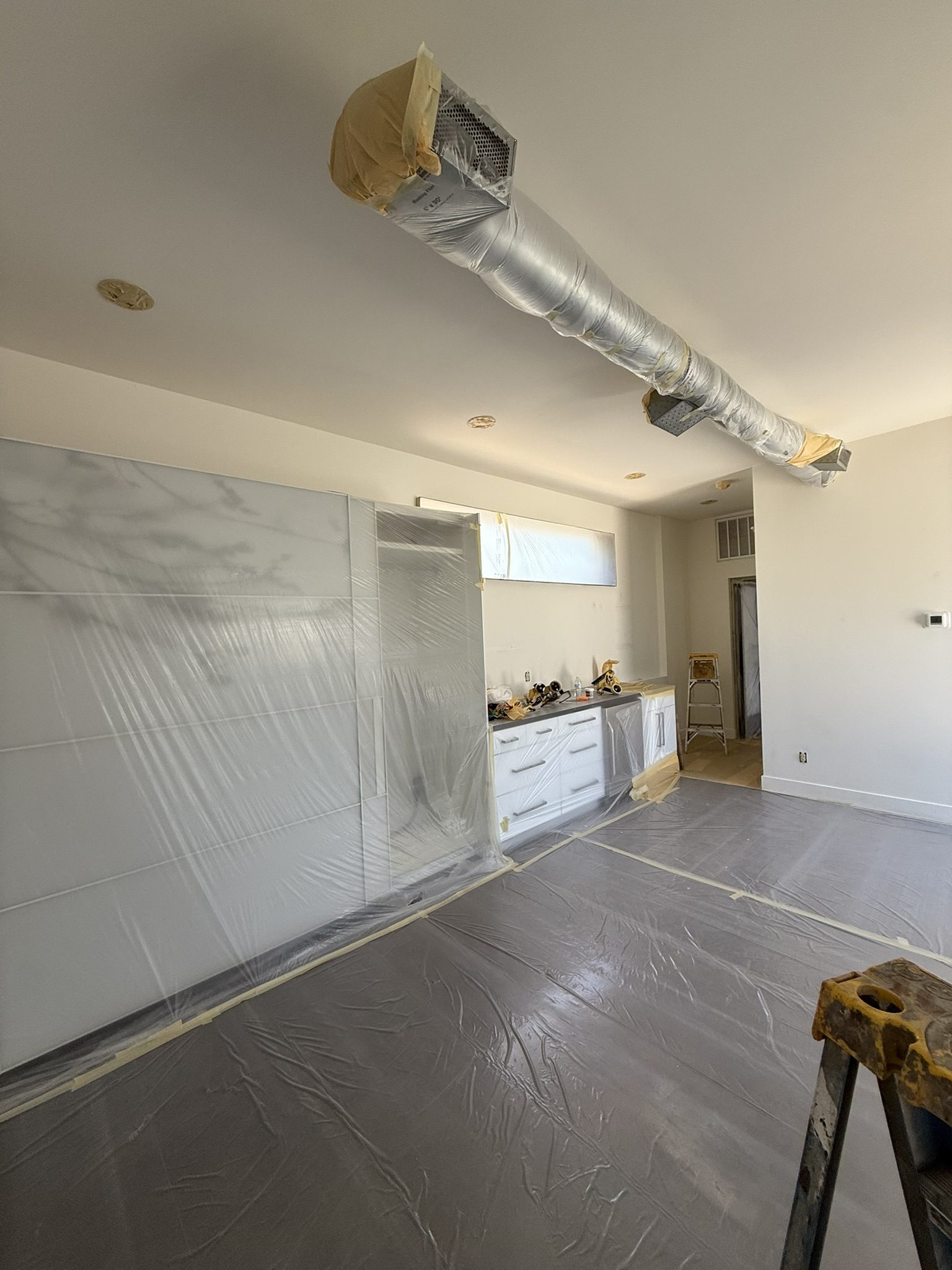 Kitchen cabinets and countertop run sheeted in plastic and taped off inside a room being prepared for interior painting
