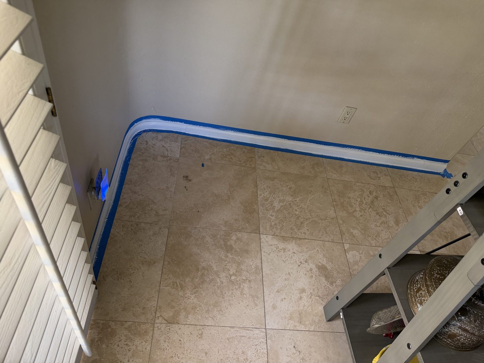 Masked and painted baseboard running past plantation shutters with a step ladder in the room