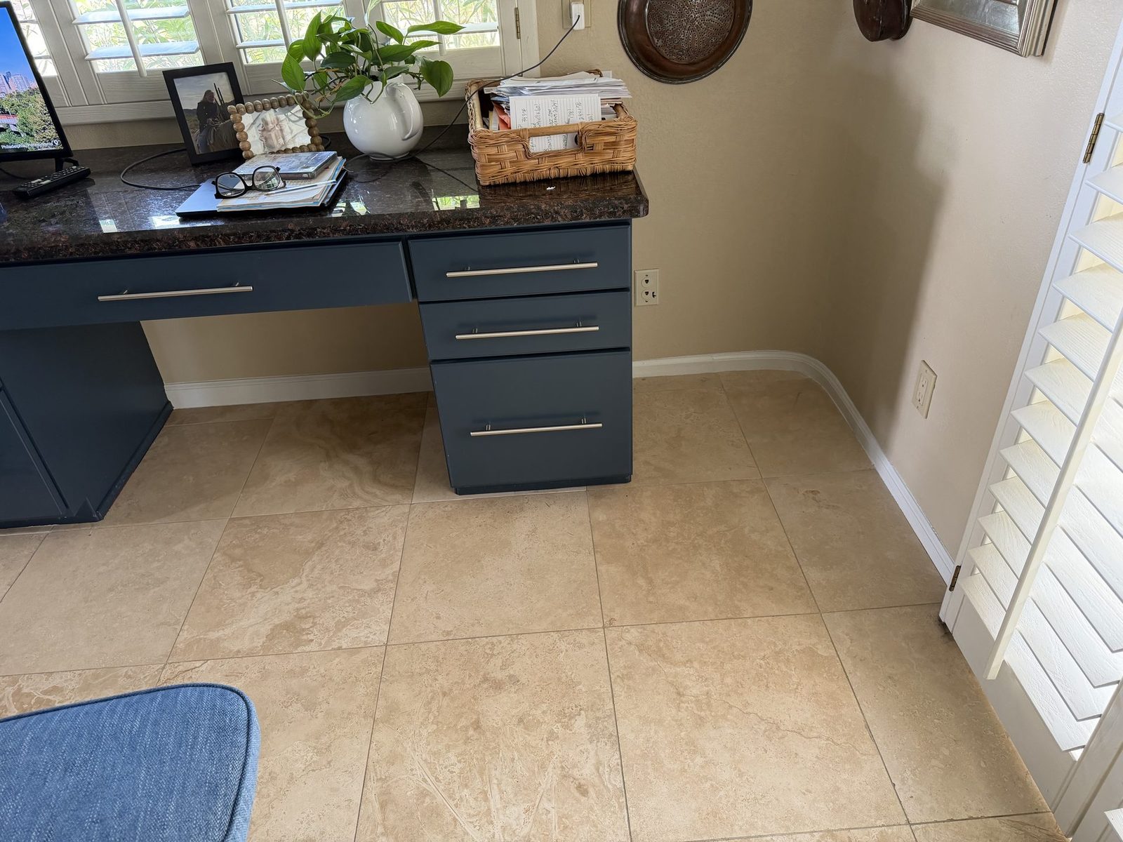 Repainted white baseboards and door casing running through a home office with a built-in navy desk on travertine tile