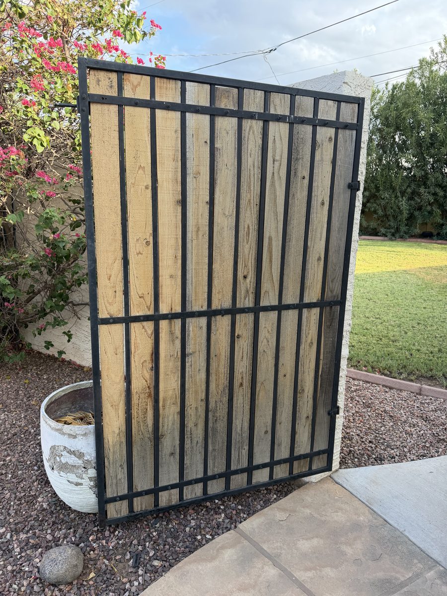 Tall iron gate with wood infill slats lifted off its hinges and leaned against a wall for preparation