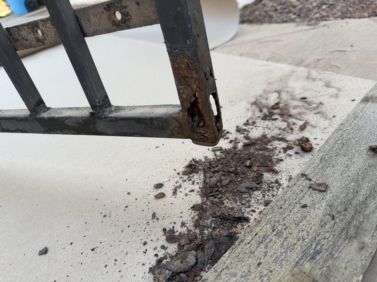 Rust scale flaking off the bottom rail of an iron gate onto concrete at a Phoenix home