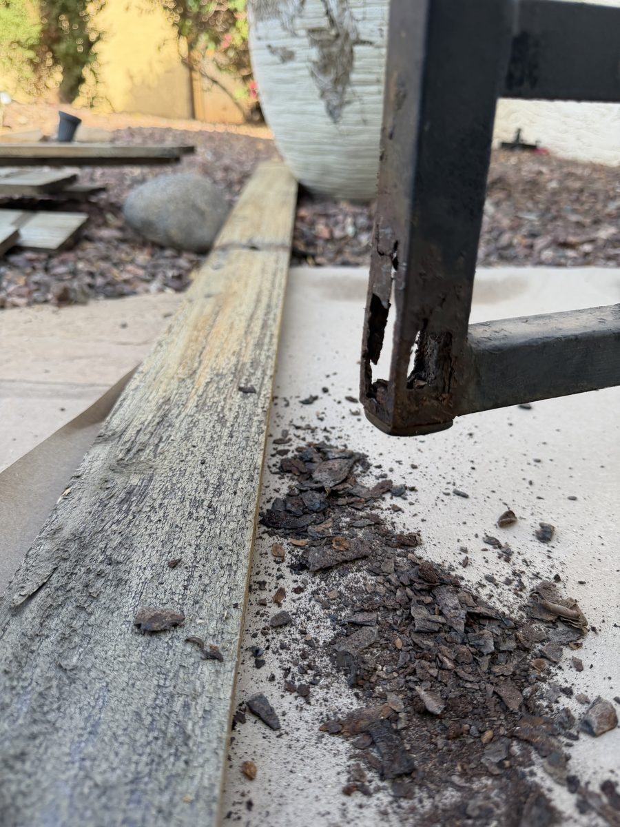 Corroded iron post base where the gate post meets concrete at a Phoenix home, with rust scale on the ground