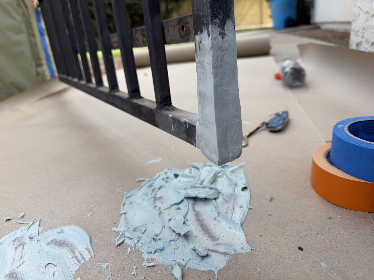 Iron railing masked with paper and tape, with two-part filler applied at the corroded post base