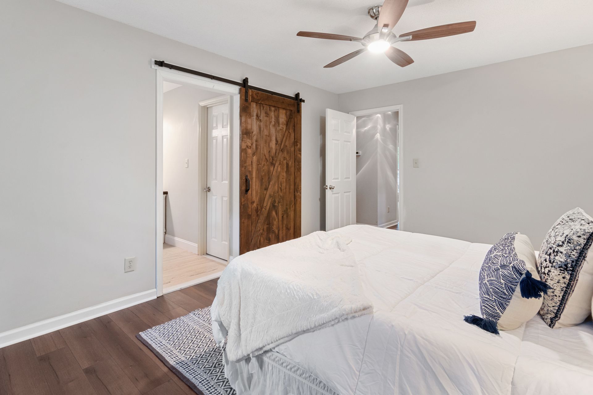 Stained knotty-wood Z-brace barn door with a black pull on a black rail, pushed aside from a trimmed opening to a hallway bath