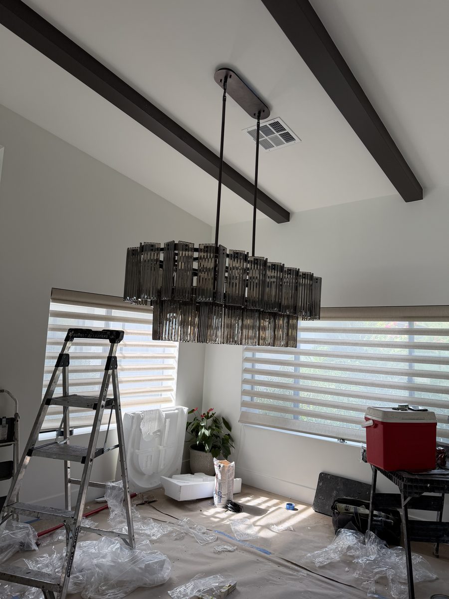 Oversized linear chandelier being installed from scaffolding in a central Phoenix dining room with drop cloths down