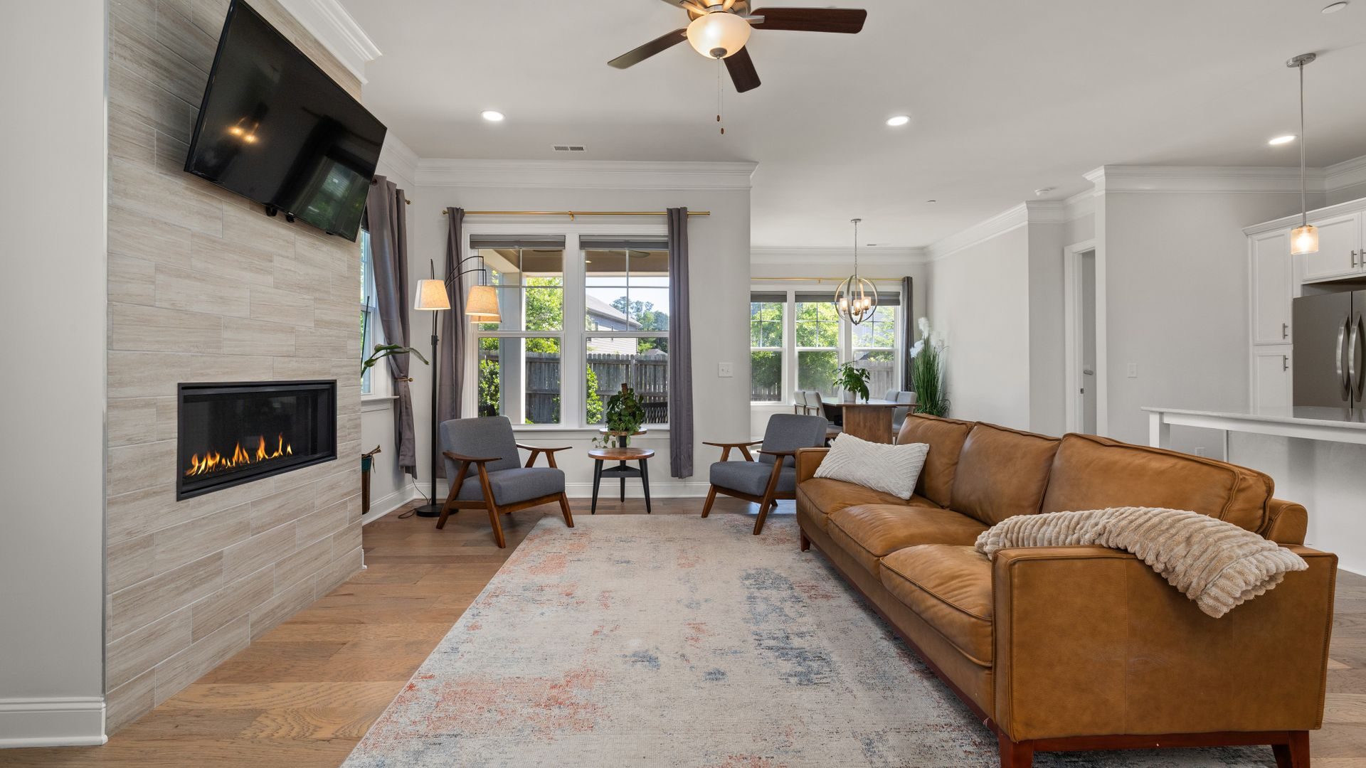 A recessed linear fireplace burning in a tiled feature wall with a TV mounted above it in a living room