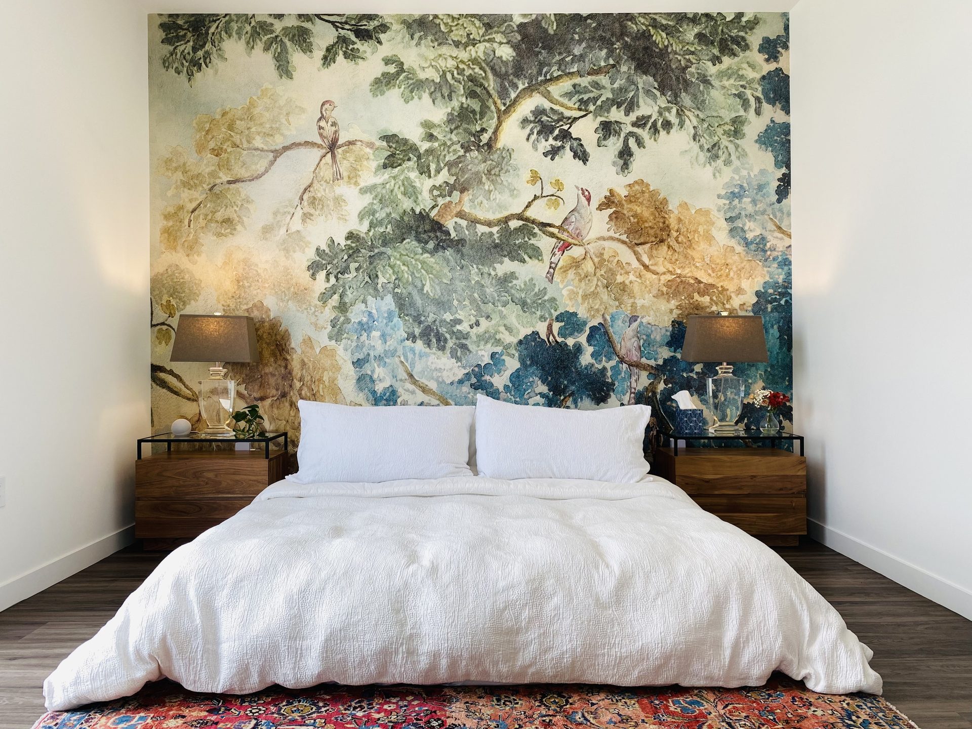 Bedroom in a downtown Phoenix condo with a large-scale botanical mural on the bed wall, low platform bed and matching walnut nightstands with lamps