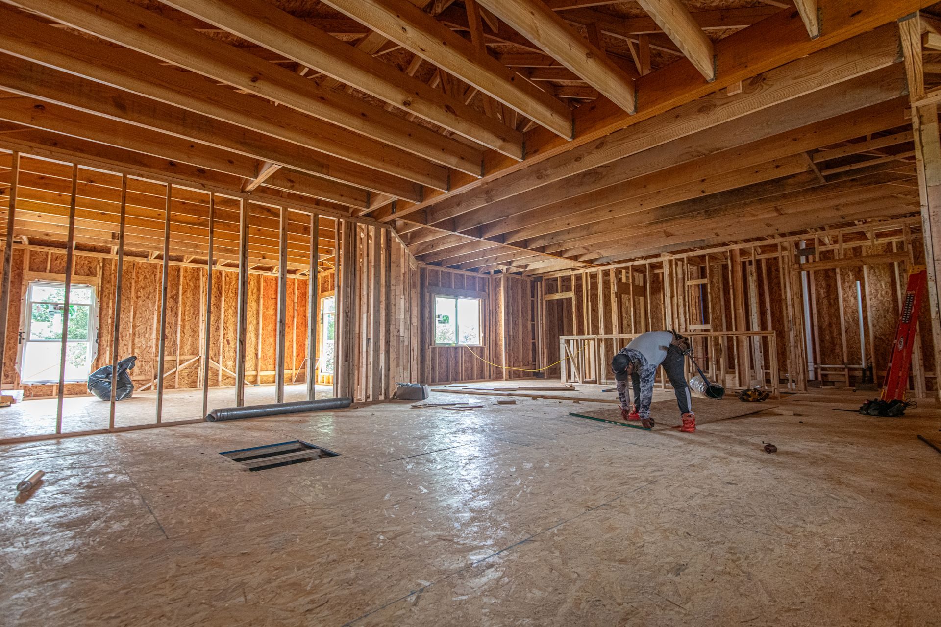 A wood stud partition with open bays framed across one side of a room under exposed ceiling joists, on an OSB subfloor, before drywall