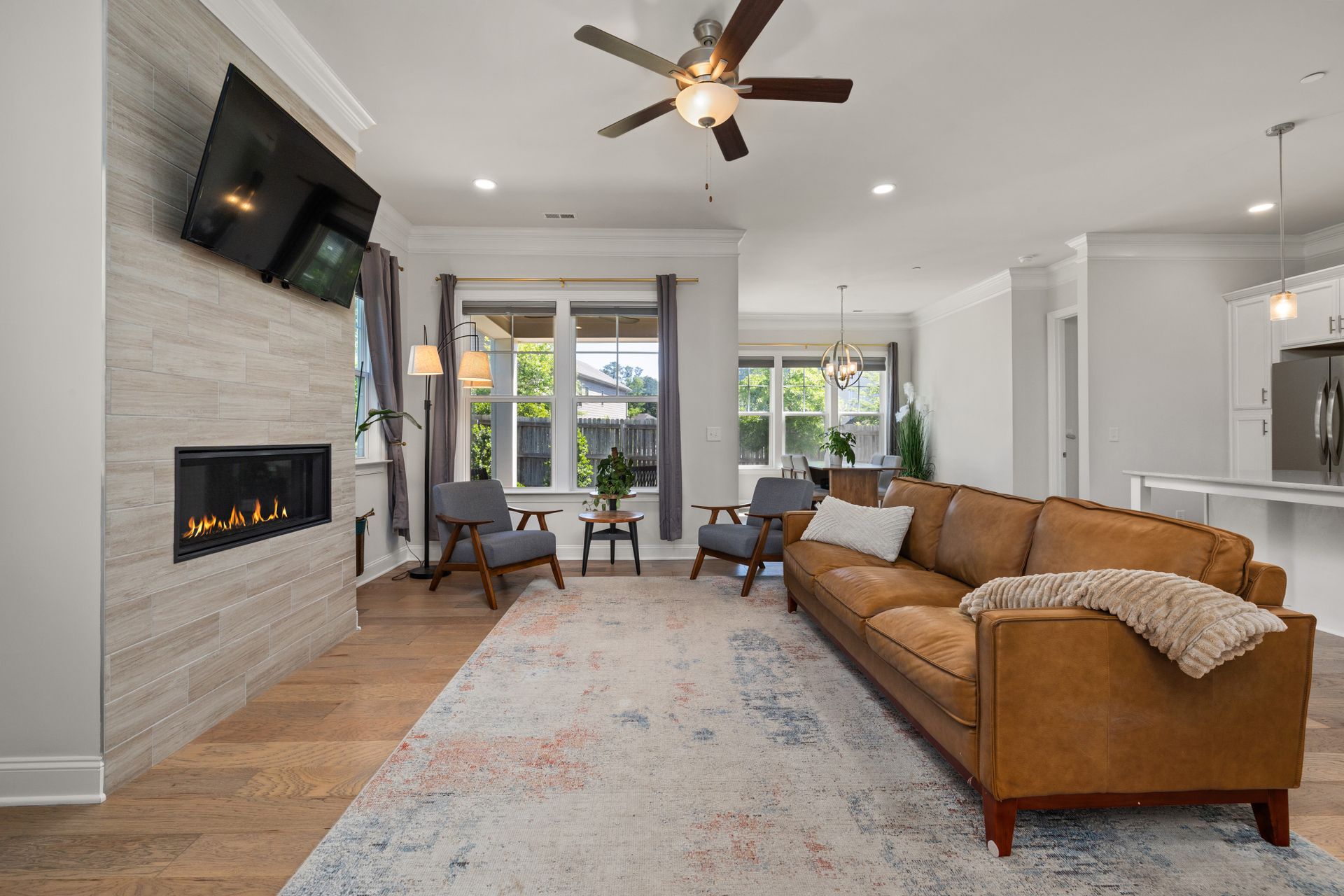 Brushed-nickel five-blade ceiling fan with dark walnut blades and a frosted glass bowl light kit in an open living room with recessed cans and a tiled fireplace wall
