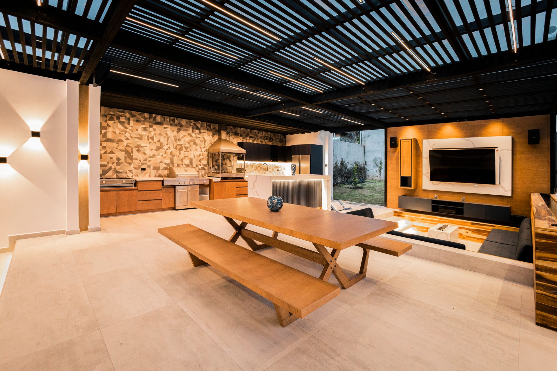 Full outdoor kitchen with a built-in grill, exhaust hood, sink, refrigerator and a long counter run under a covered patio