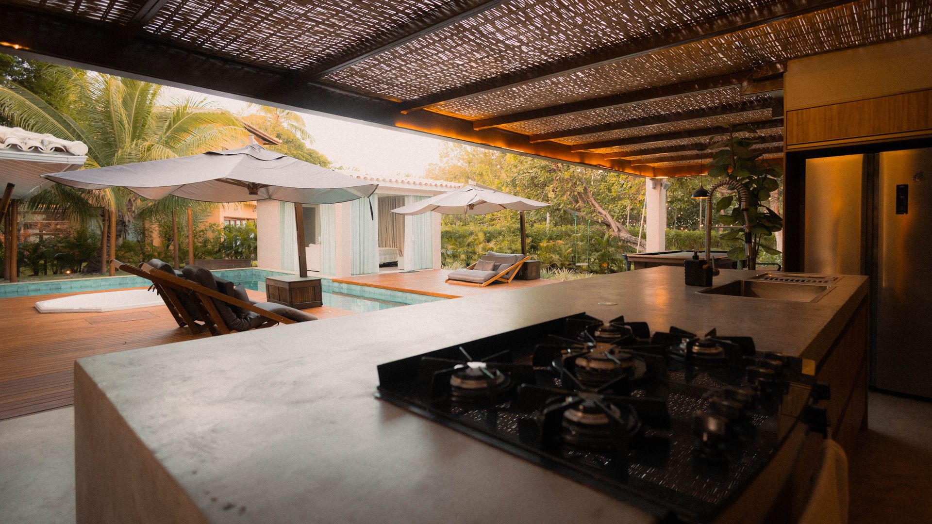 Outdoor kitchen with a concrete counter, built-in gas cooktop and sink beside a pool