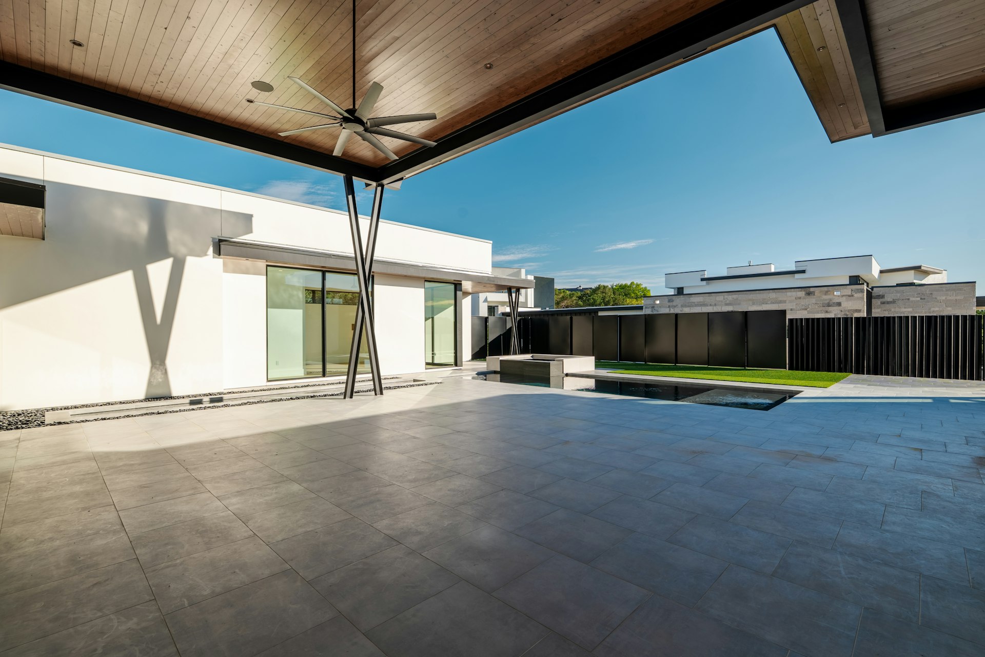 Underside of a solid patio roof with a tongue and groove wood ceiling and a large ceiling fan above a large-format paver deck