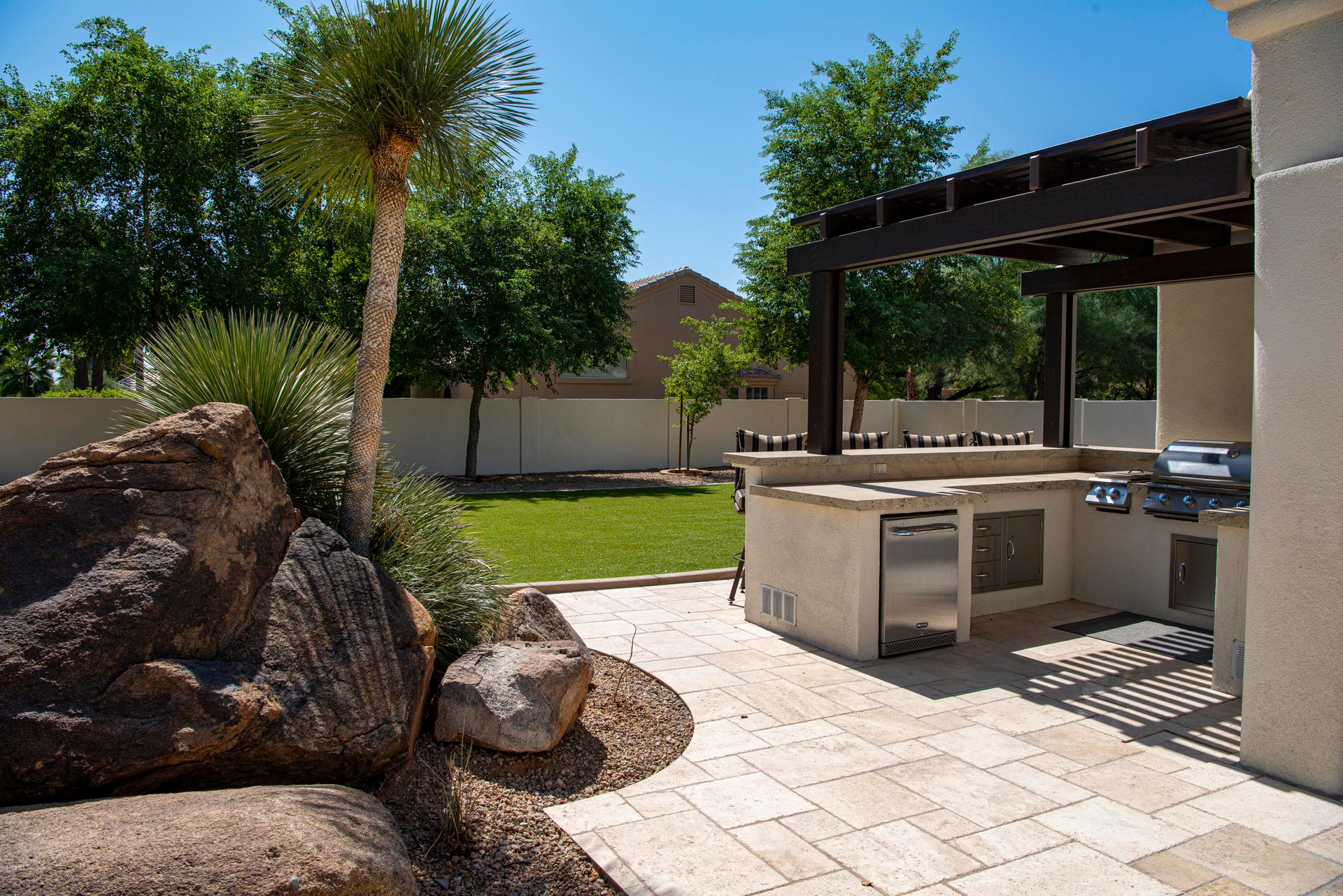 Dark aluminum pergola over an outdoor kitchen and travertine patio