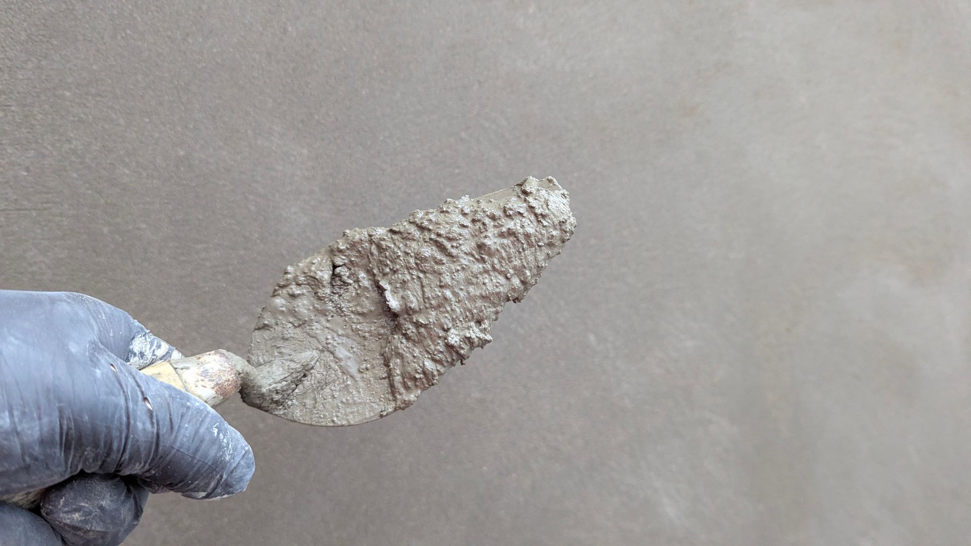 Gloved hand applying plaster to an interior wall with a steel trowel