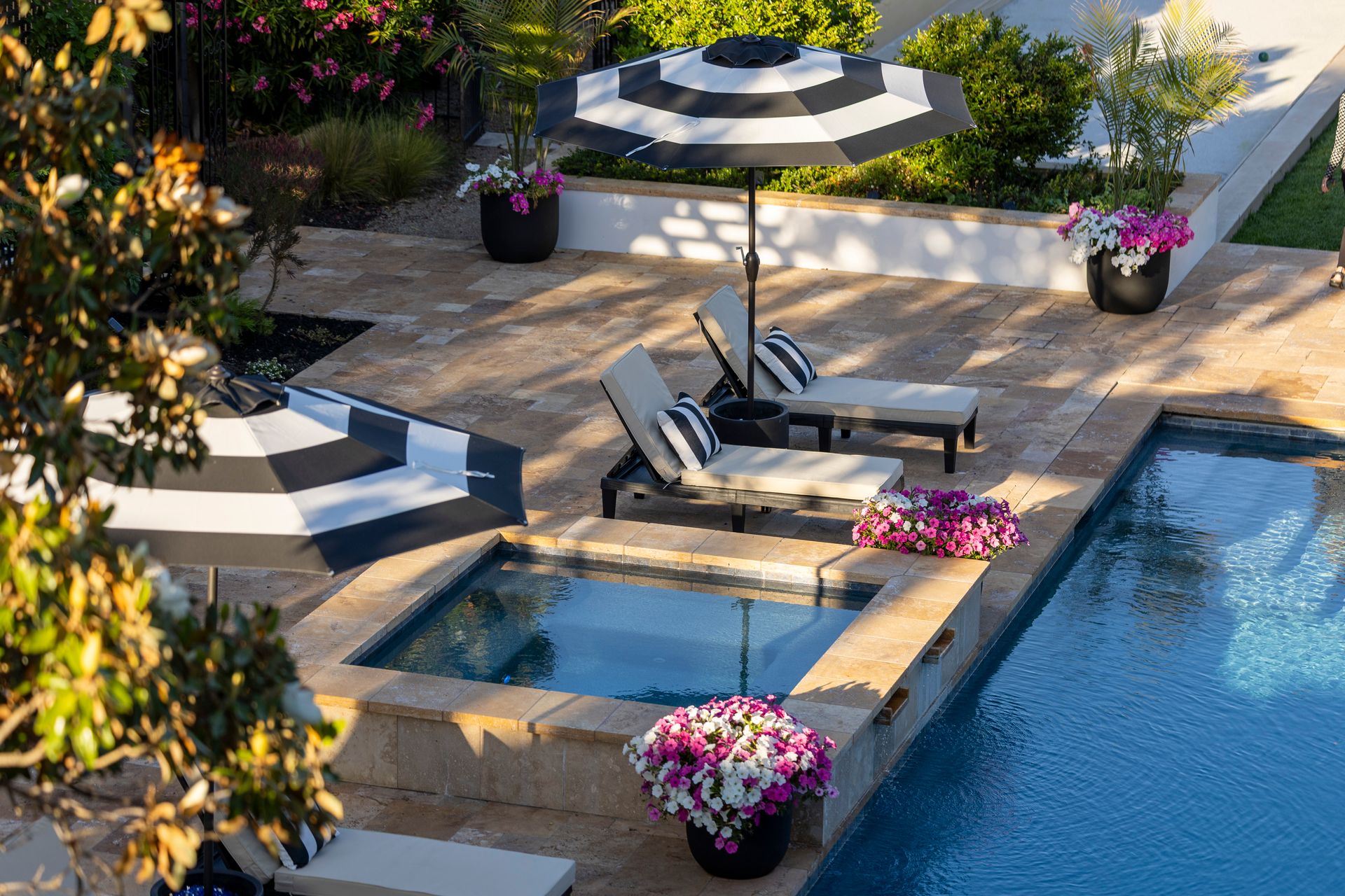 Travertine paver deck and coping around a raised spa and pool, with lounge chairs and striped umbrellas
