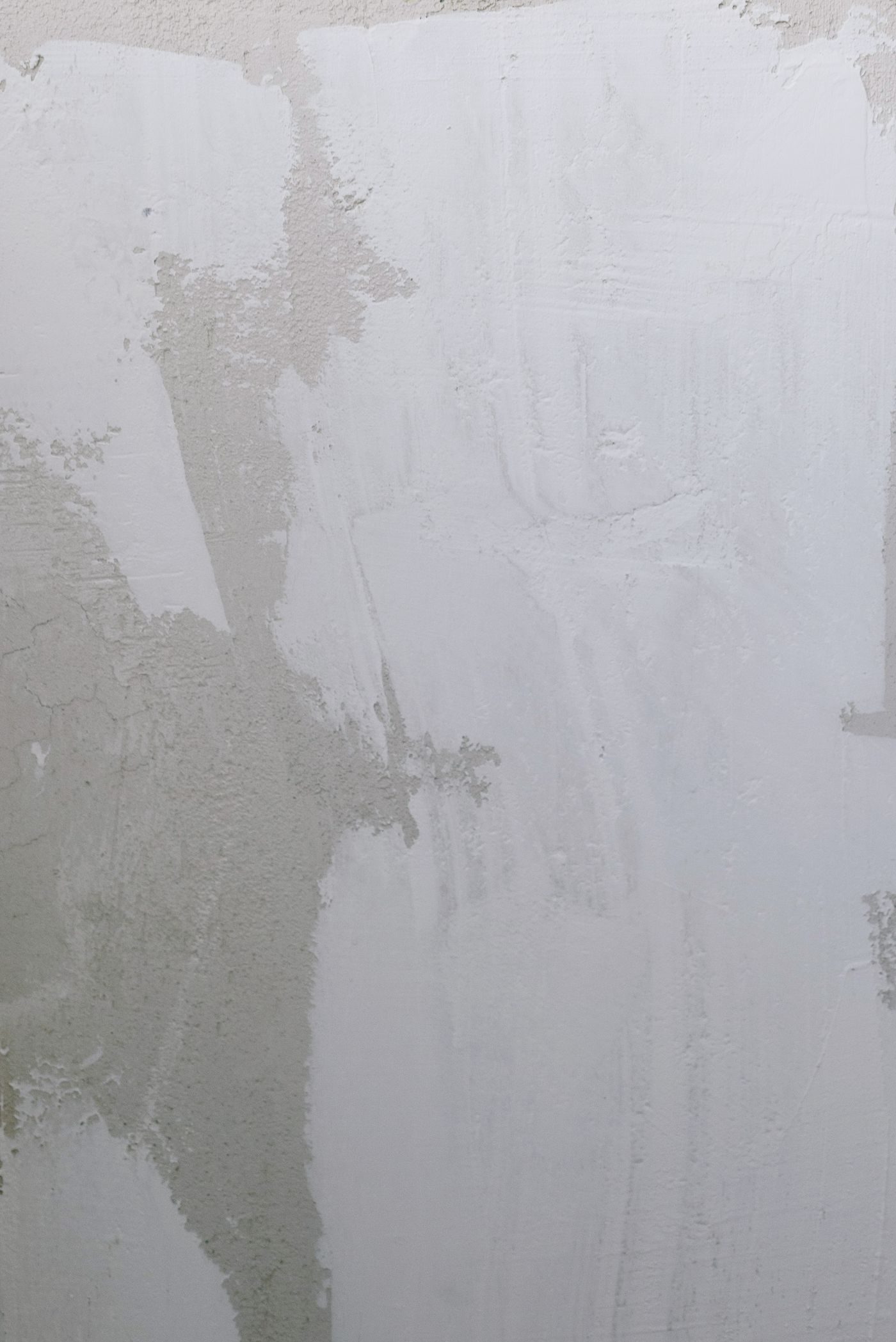 Wall surface showing thin hairline cracks and patched areas that have dried to a different sheen than the wall around them