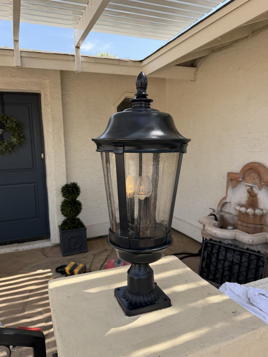 Refinished black pier-mount lantern lit with a warm bulb behind seeded glass on a stone column