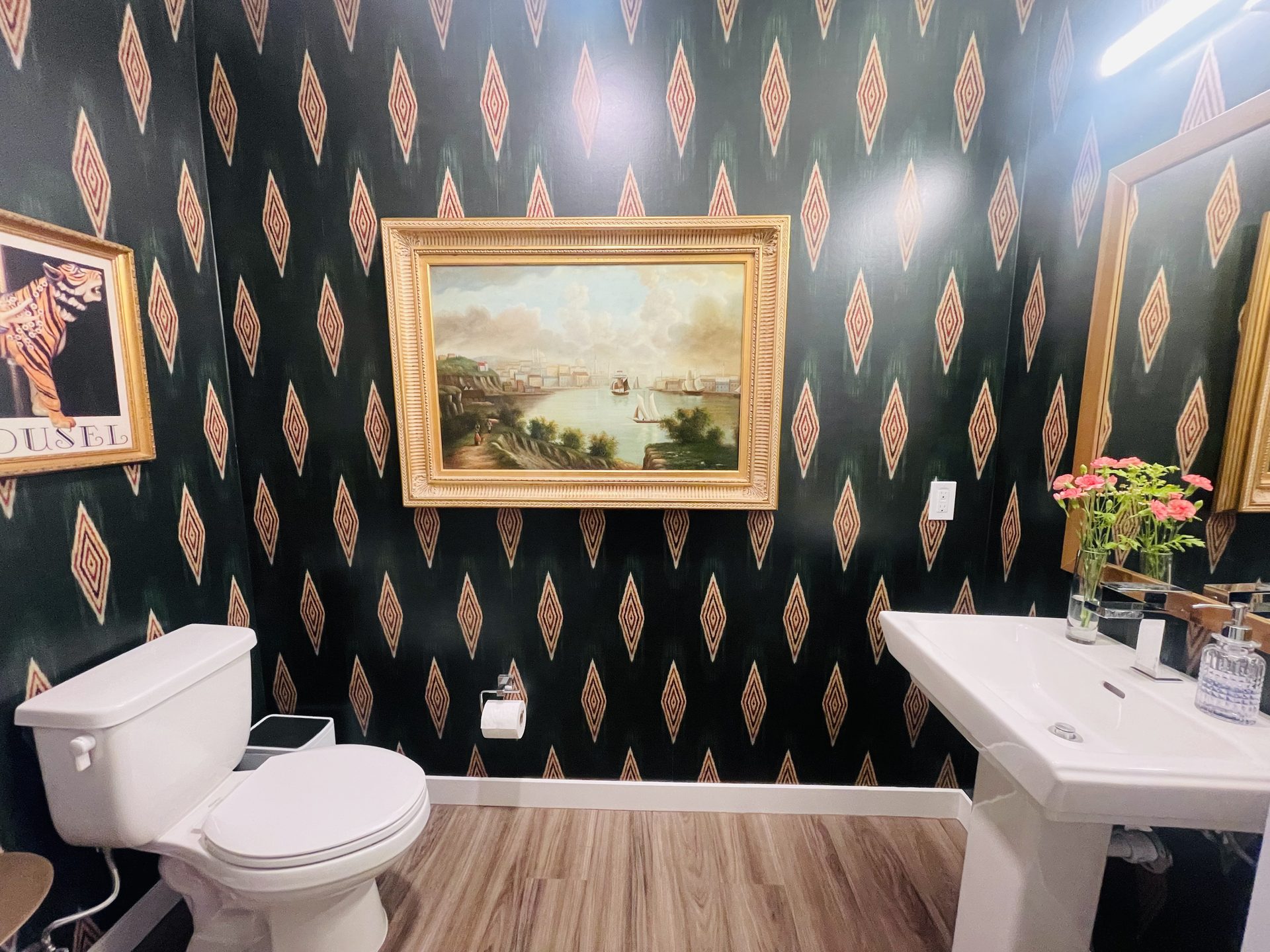 Powder room in a downtown Phoenix condo papered in a dark green repeating diamond pattern, with a gold-framed landscape painting centered on the main wall