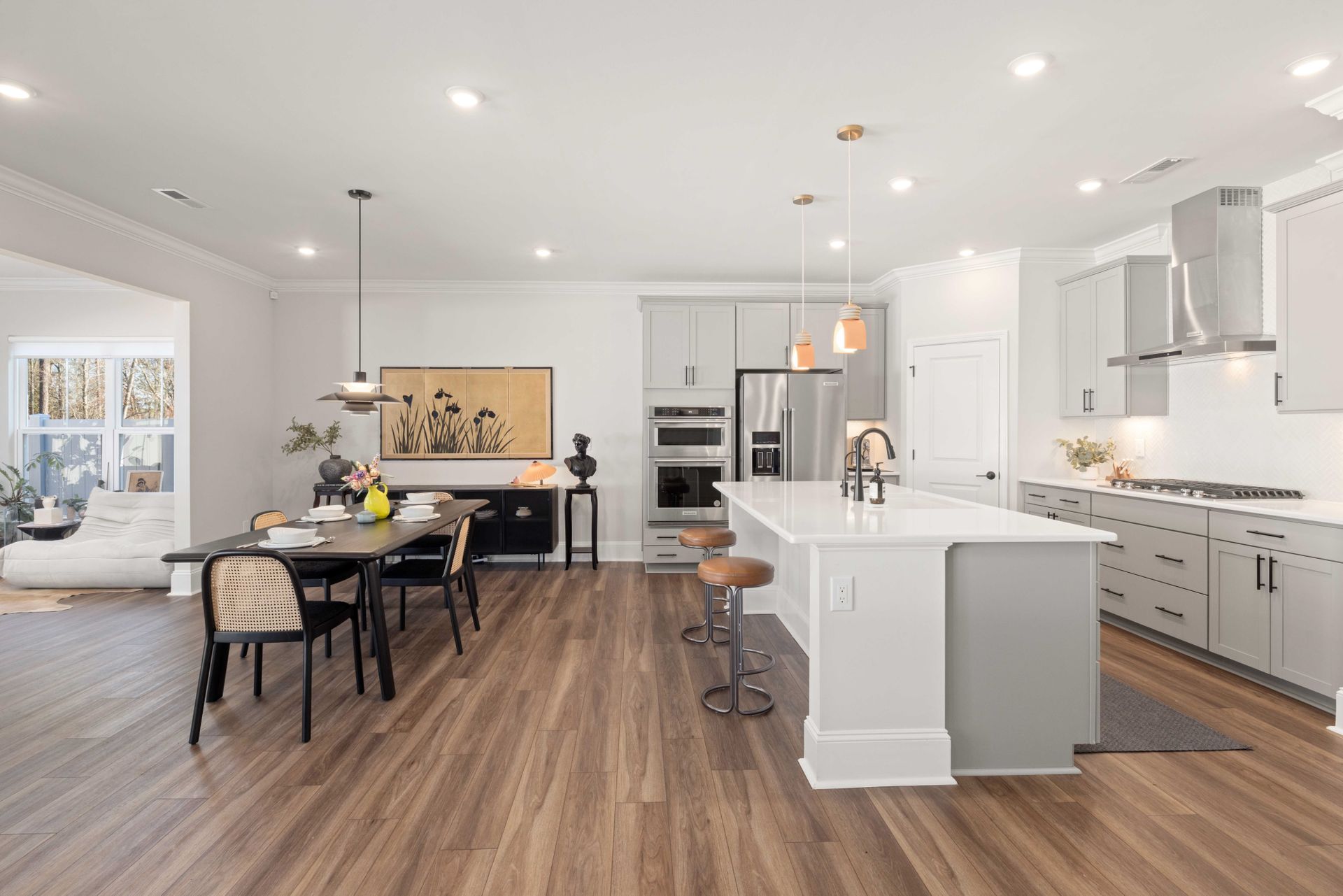 Kitchen and dining room with evenly spaced slim round recessed LED downlights in a flat white ceiling and brass-stem pendants over a white quartz island