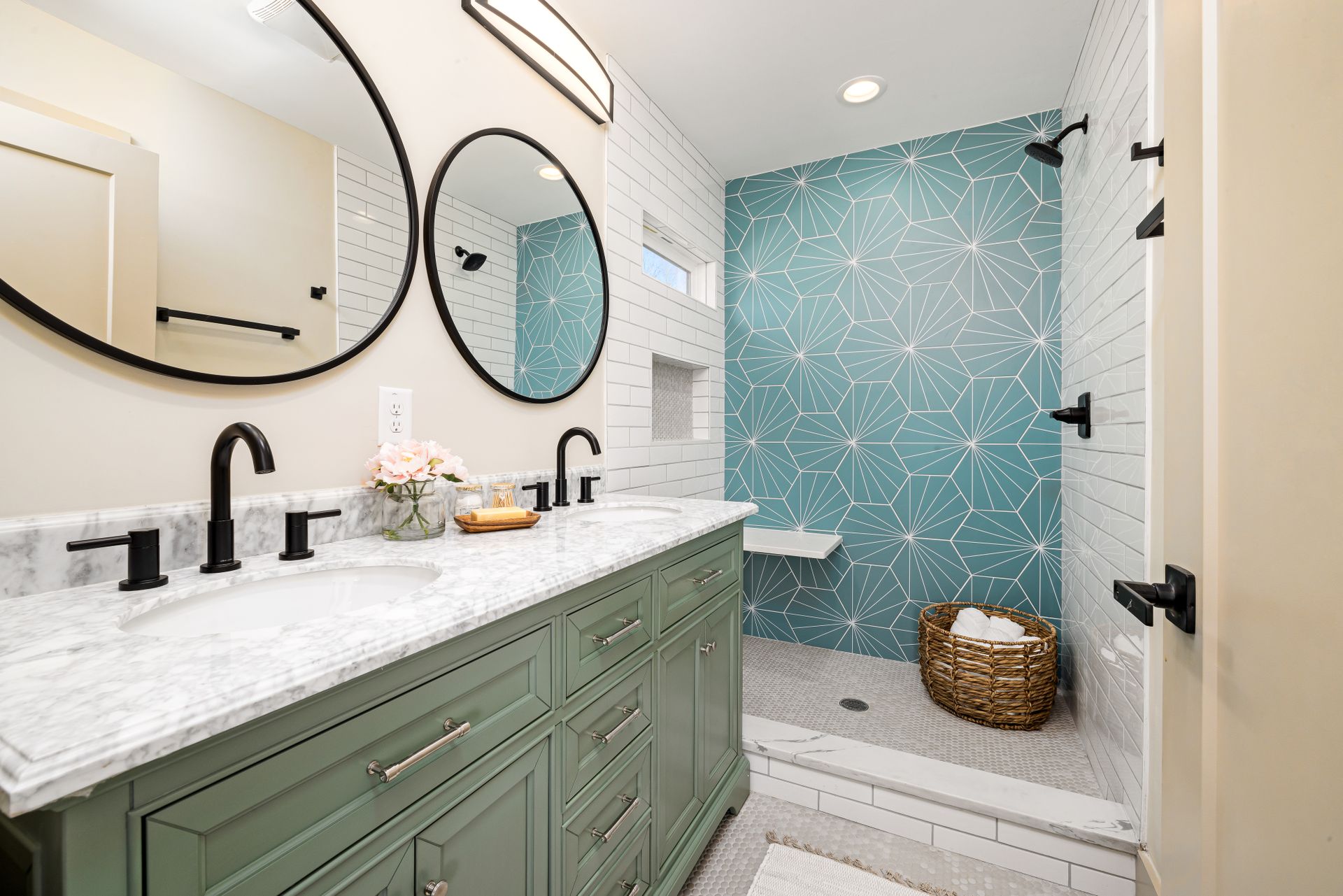 Hall bathroom with a sage-green double vanity, a Carrara-style marble top, matte-black faucets, round black-framed mirrors and a black bar light, with a walk-in shower and penny-tile floor beyond