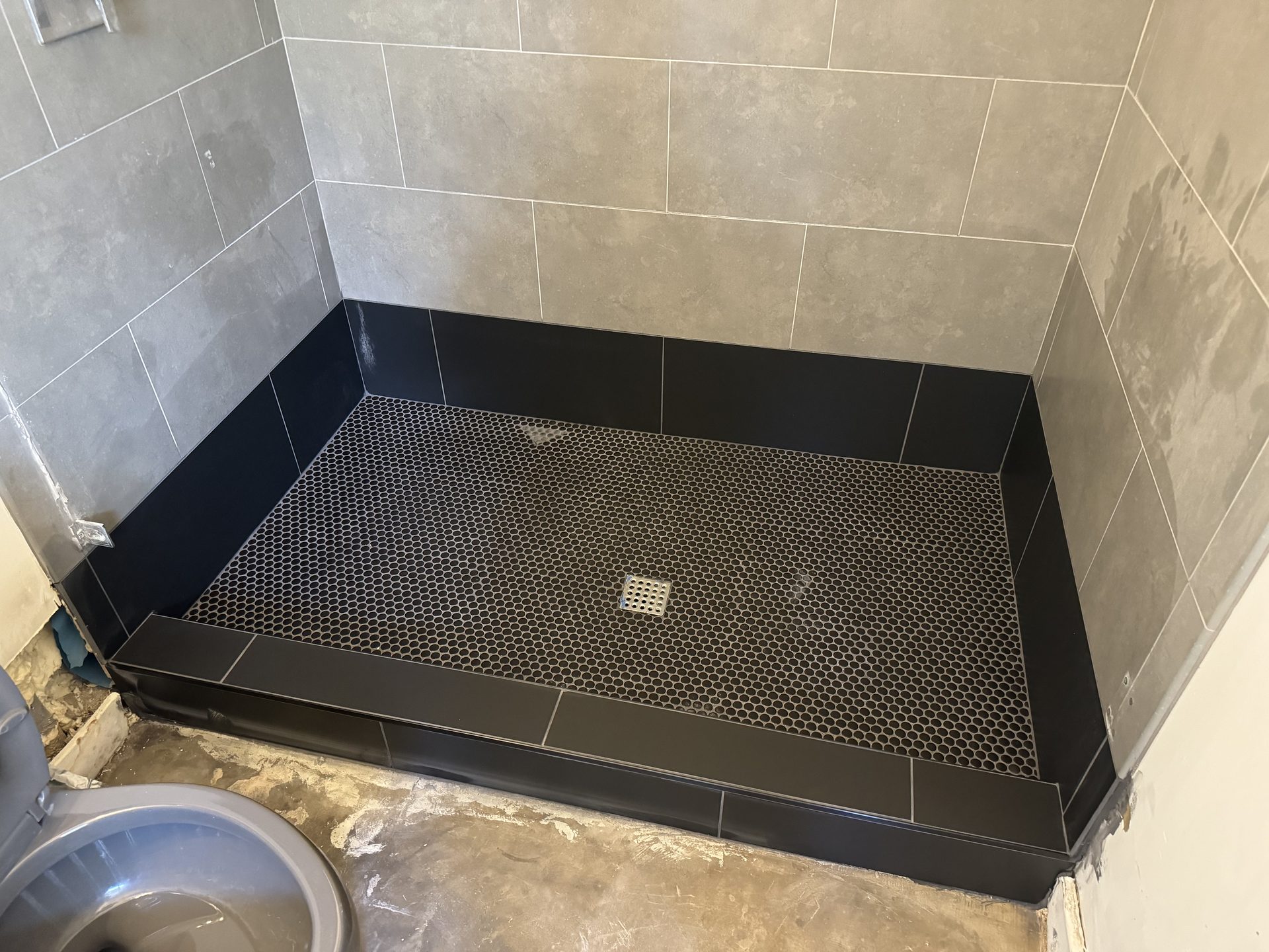 The finished rebuilt shower pan: black penny-tile floor, new bottom course and curb, existing wall tile saved