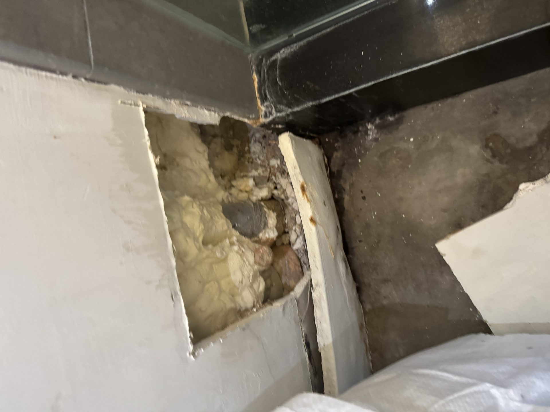 Wall opened outside the shower confirming the pan leak, water damage visible at the base