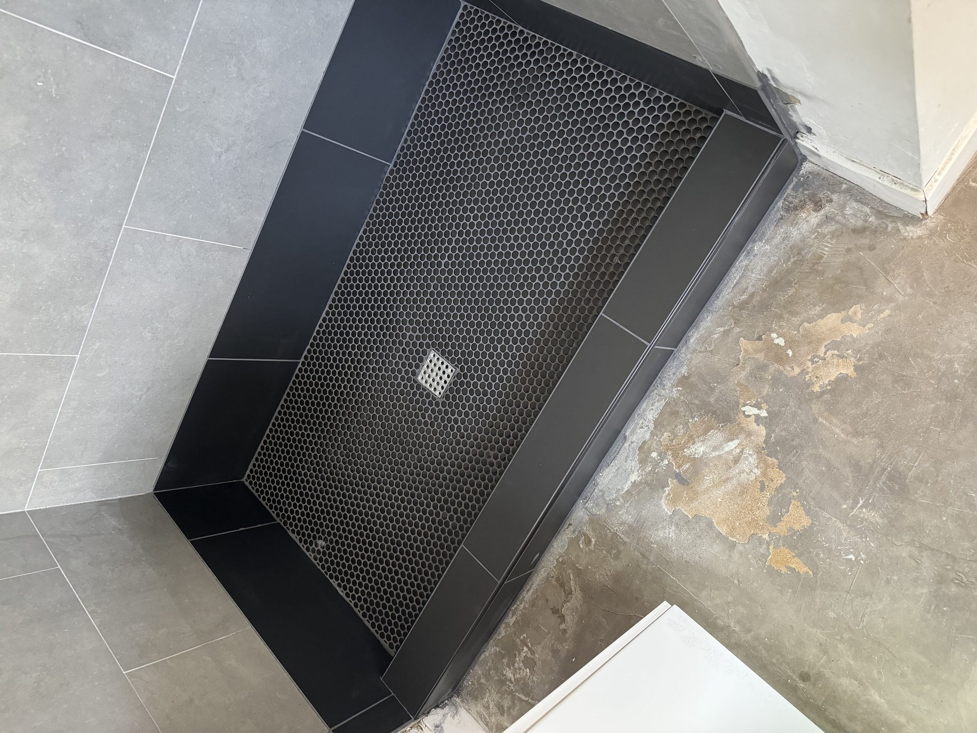 A rebuilt tiled shower pan in black penny tile with new drain, by a licensed Phoenix contractor