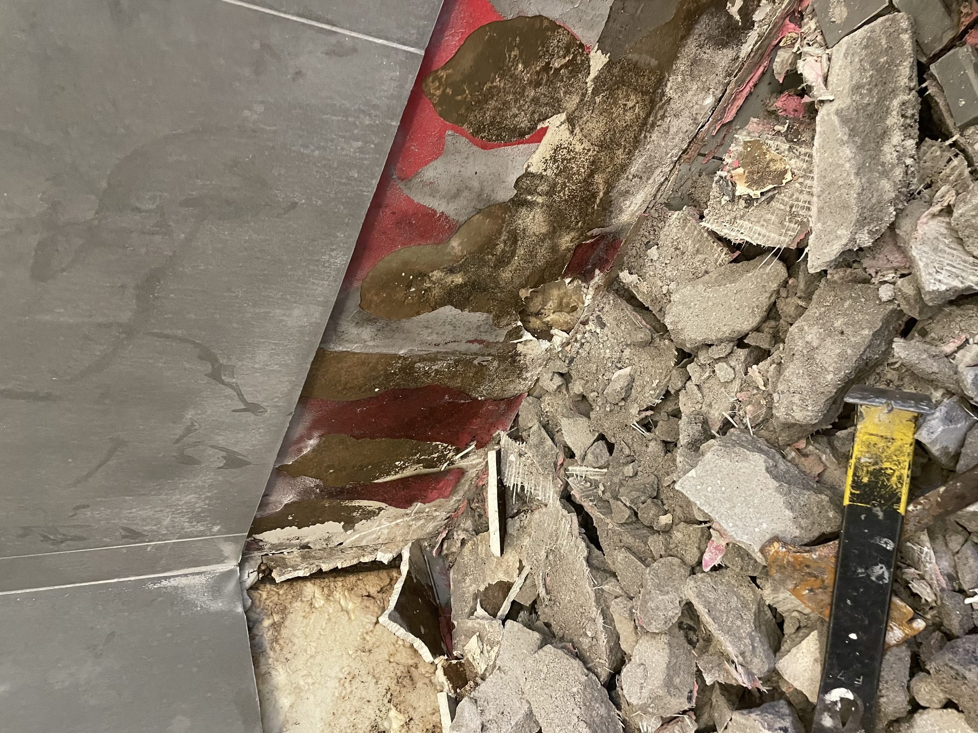 Demolition of the failed shower pan showing water staining wicked up the wall waterproofing above the bottom tile row