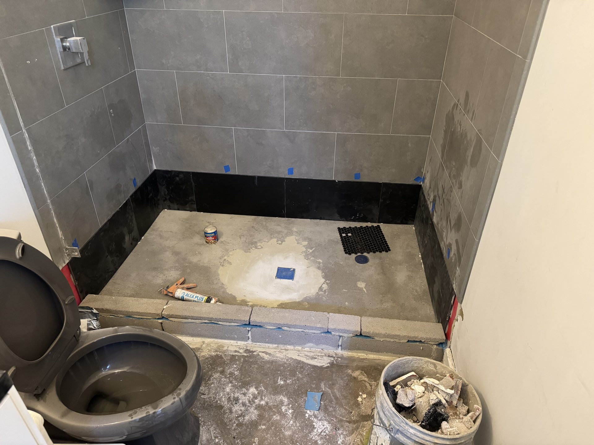 Shower pan rebuild in progress: new mortar bed, black bottom tile course, and curb, with the existing wall tile saved