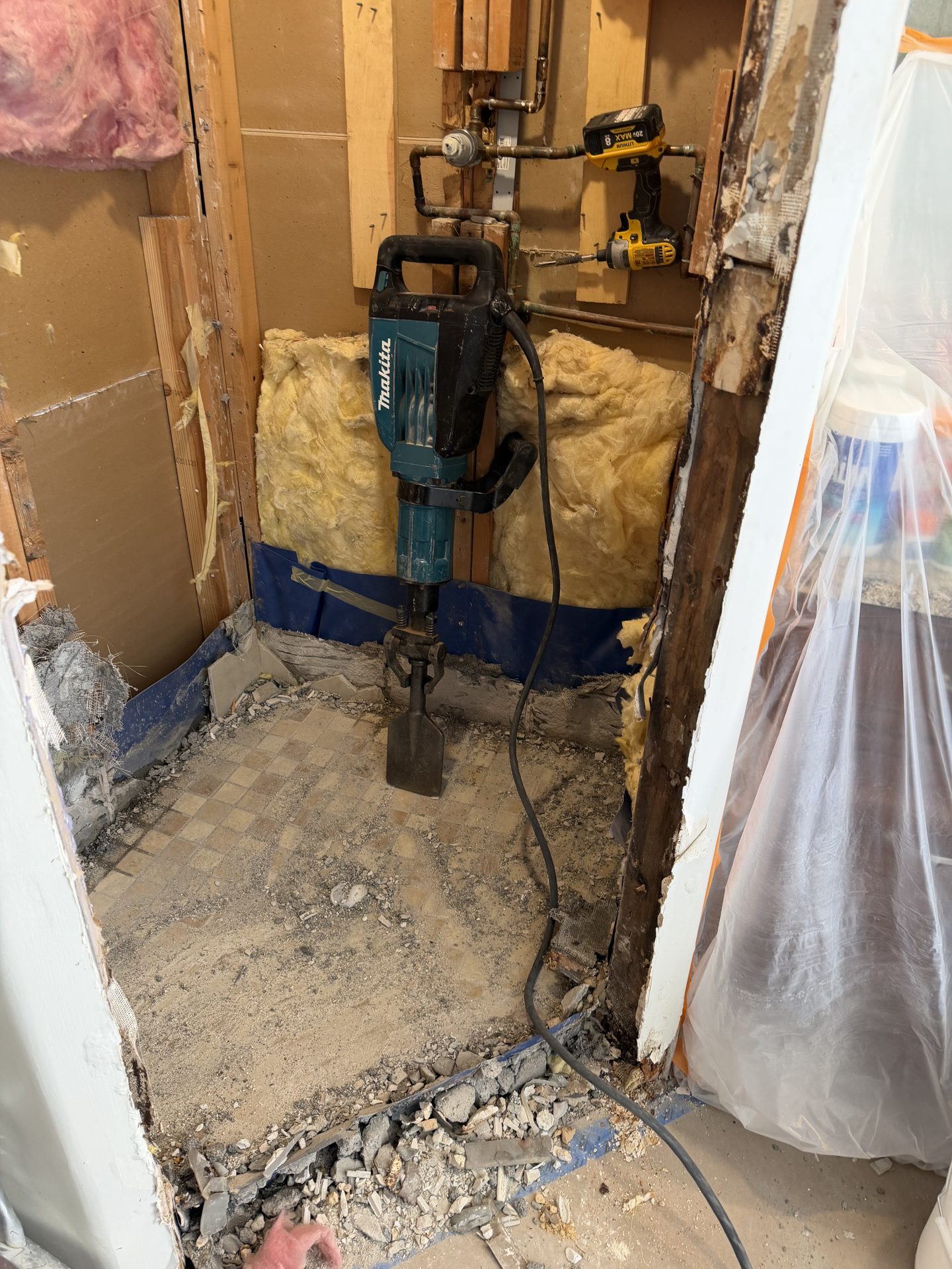 Demo hammer breaking out the failed mortar bed of a shower in a McCormick Ranch home, Scottsdale, with the walls opened to the studs