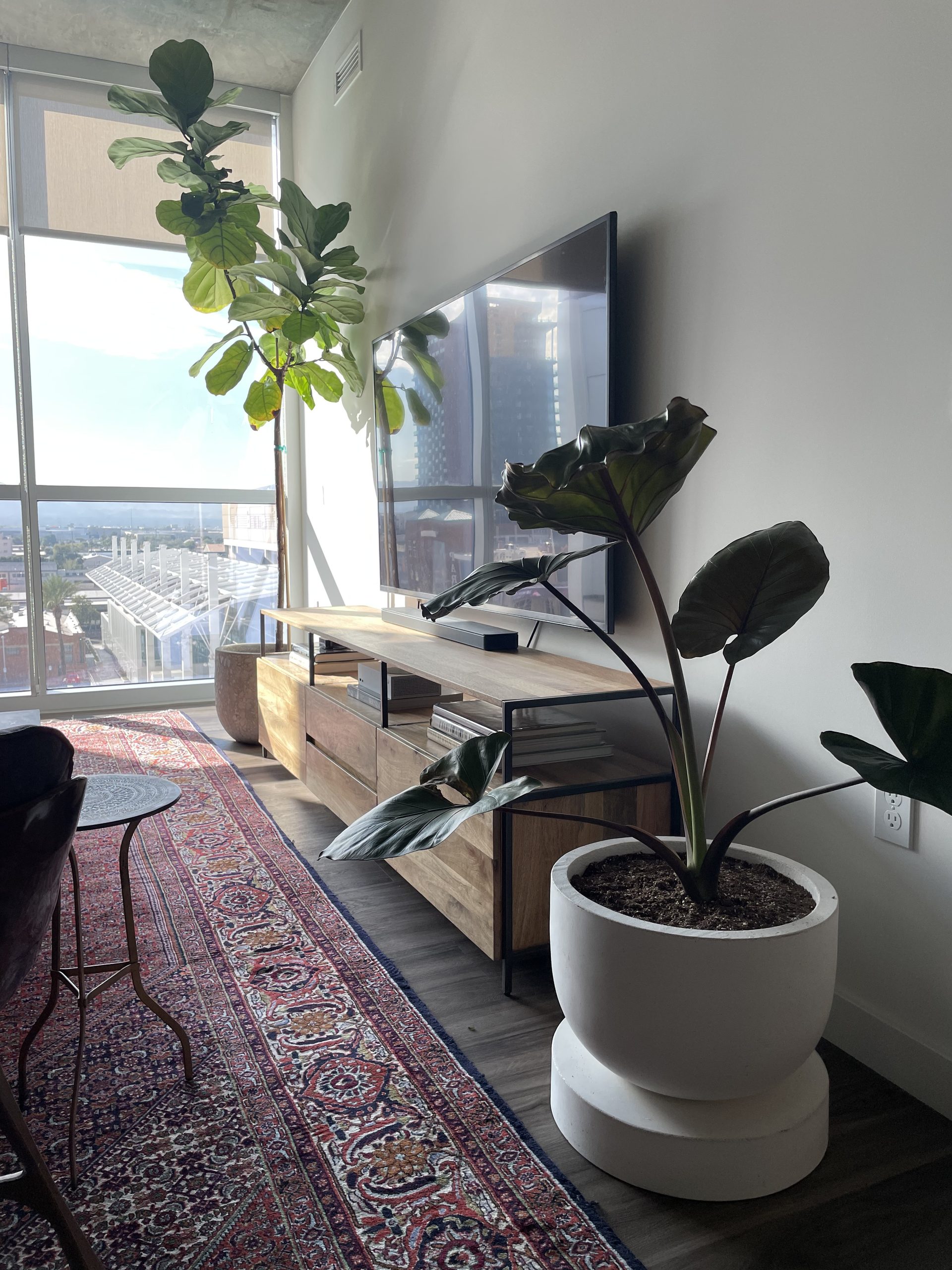 TV mounted low and tight above a long oak media console in a downtown Phoenix condo, with the soundbar on the console and the city skyline through the window